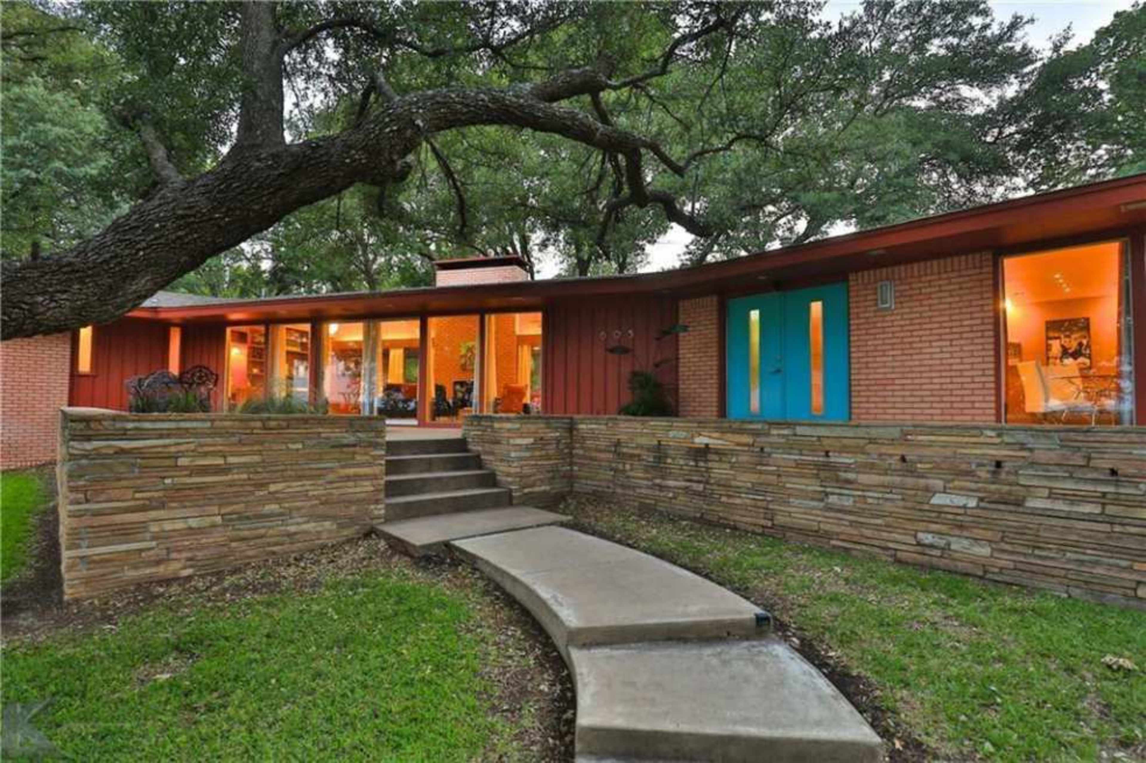 A modern home with large windows and a stone walkway is set among lush greenery.