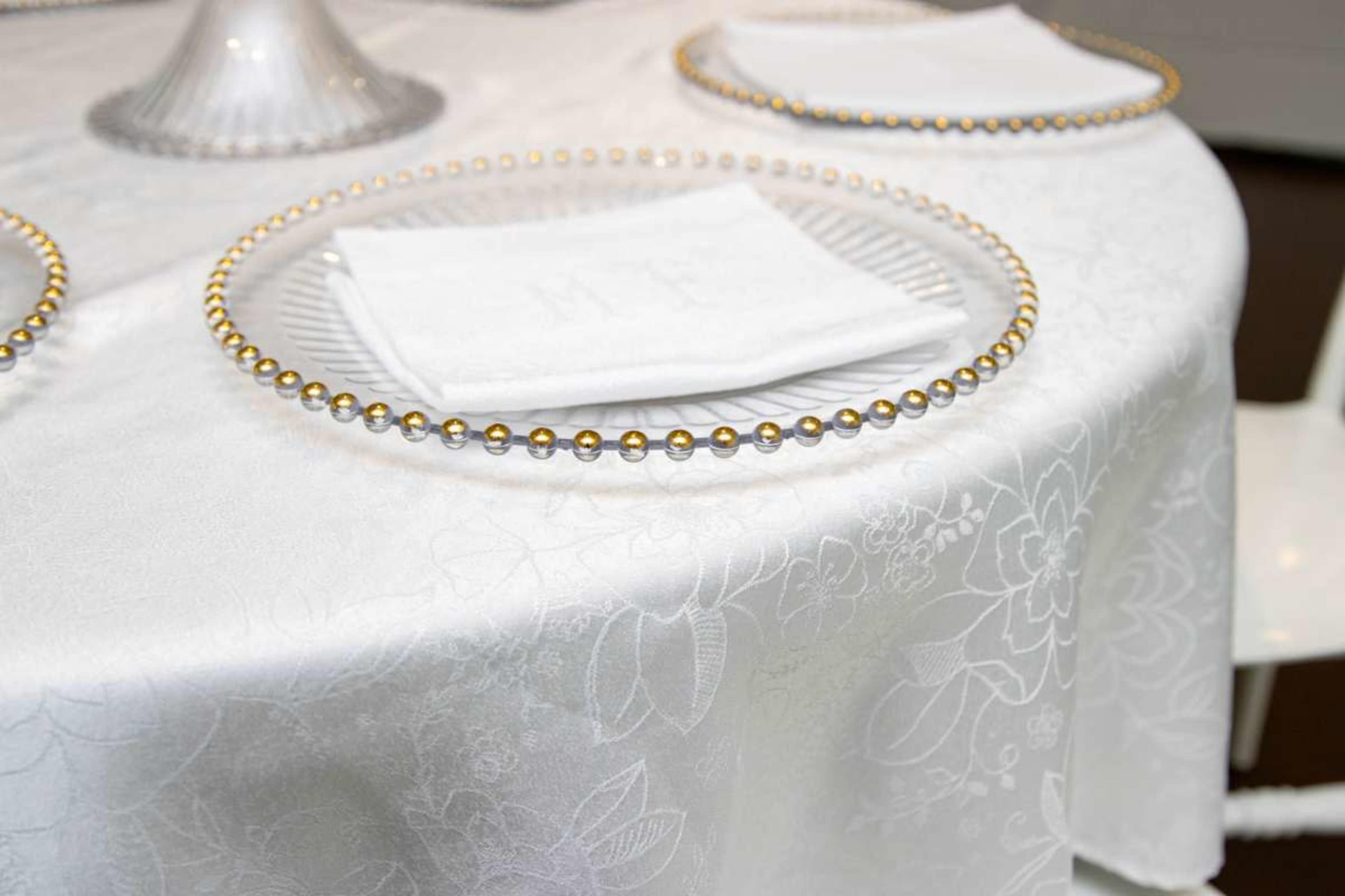 The image shows a neatly arranged dining table with a white tablecloth, decorative plates, and folded napkins placed on top.