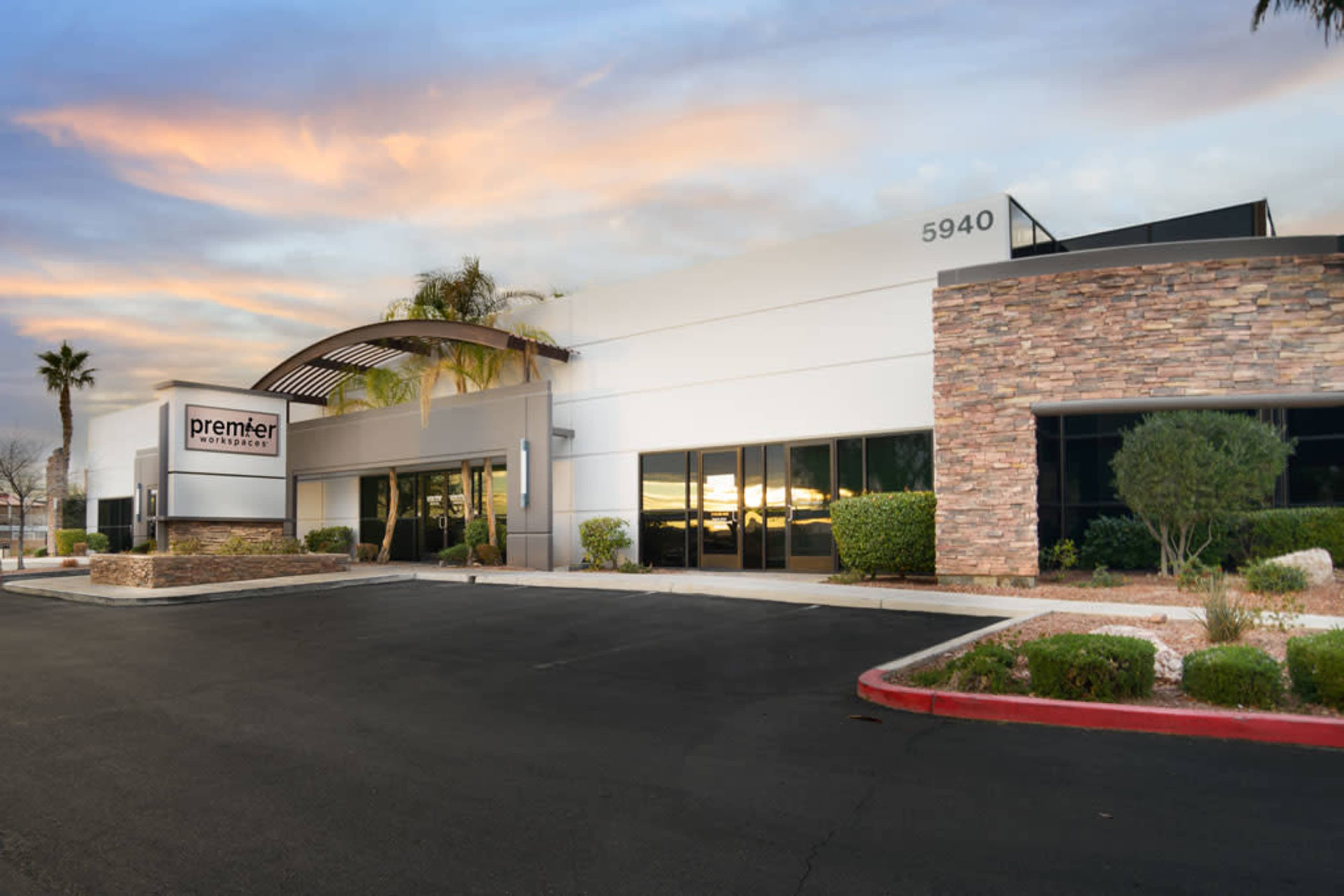 A modern commercial building with a stone-accented facade and a large sign that reads "premier," positioned in an area with palm trees and a colorful sky at sunset.