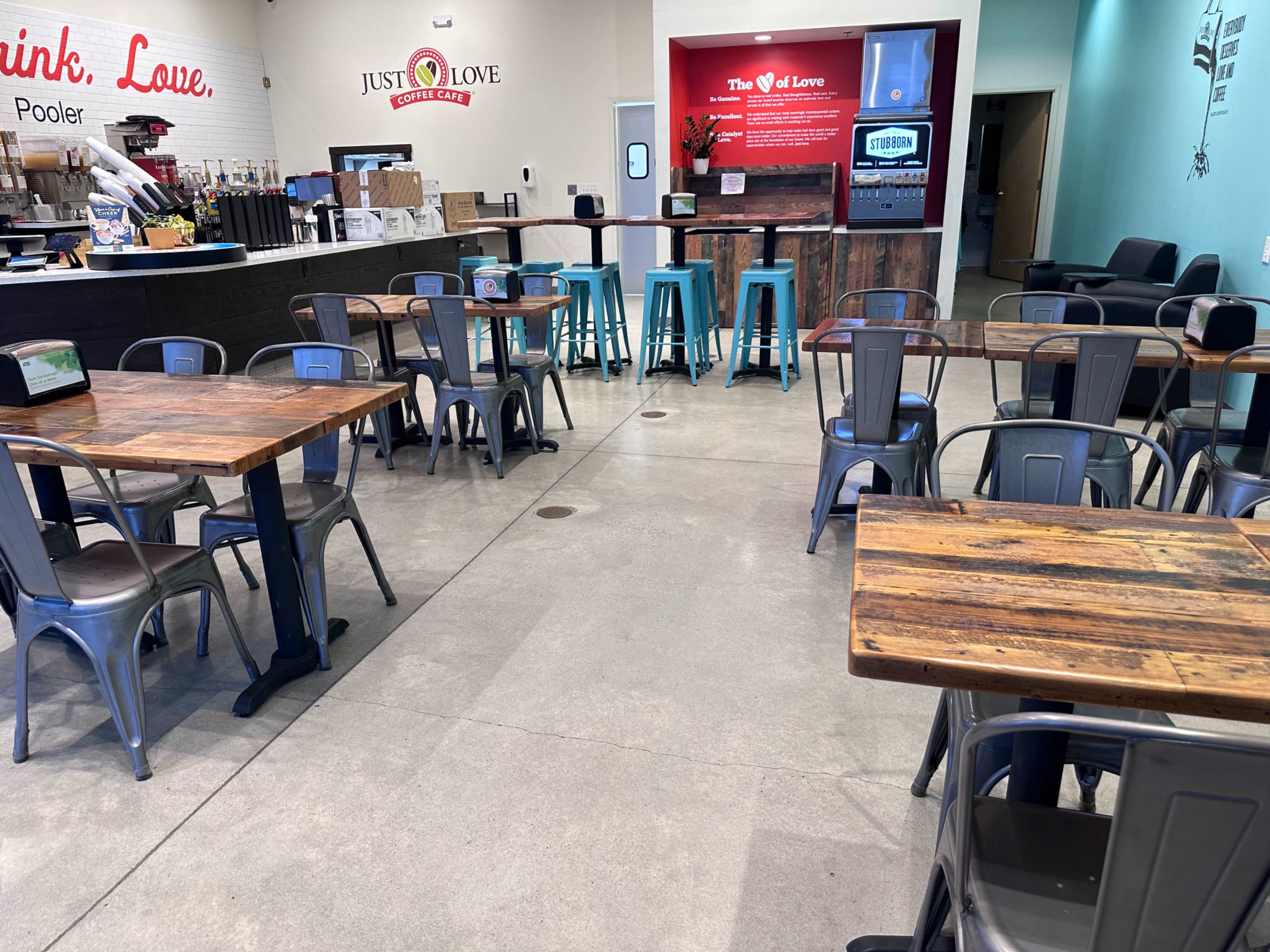 A spacious café interior with wooden tables, metal chairs, and a service counter in the background.