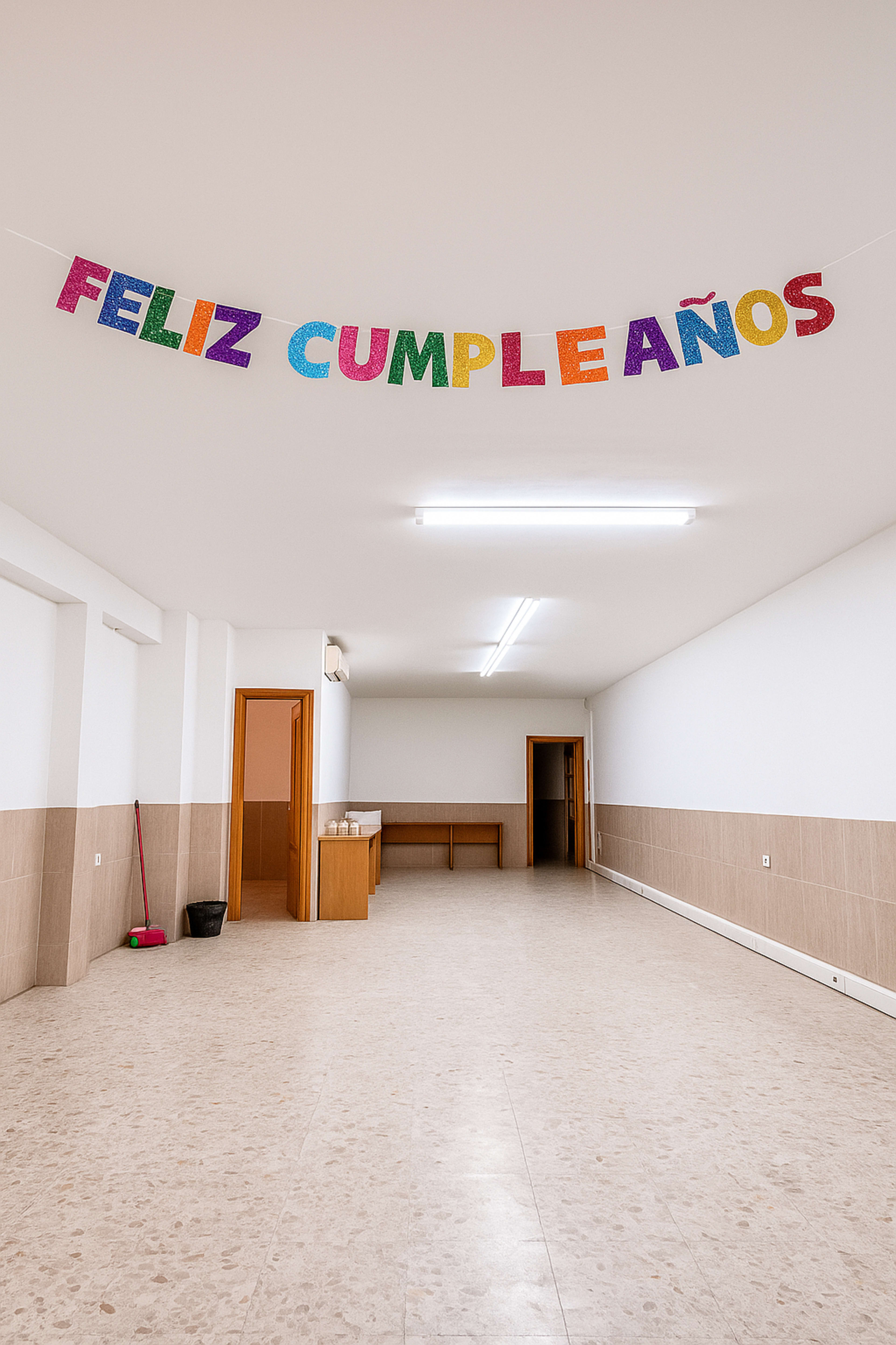 The image shows an empty room with a banner reading "FELIZ CUMPLEAÑOS" hanging from the ceiling.