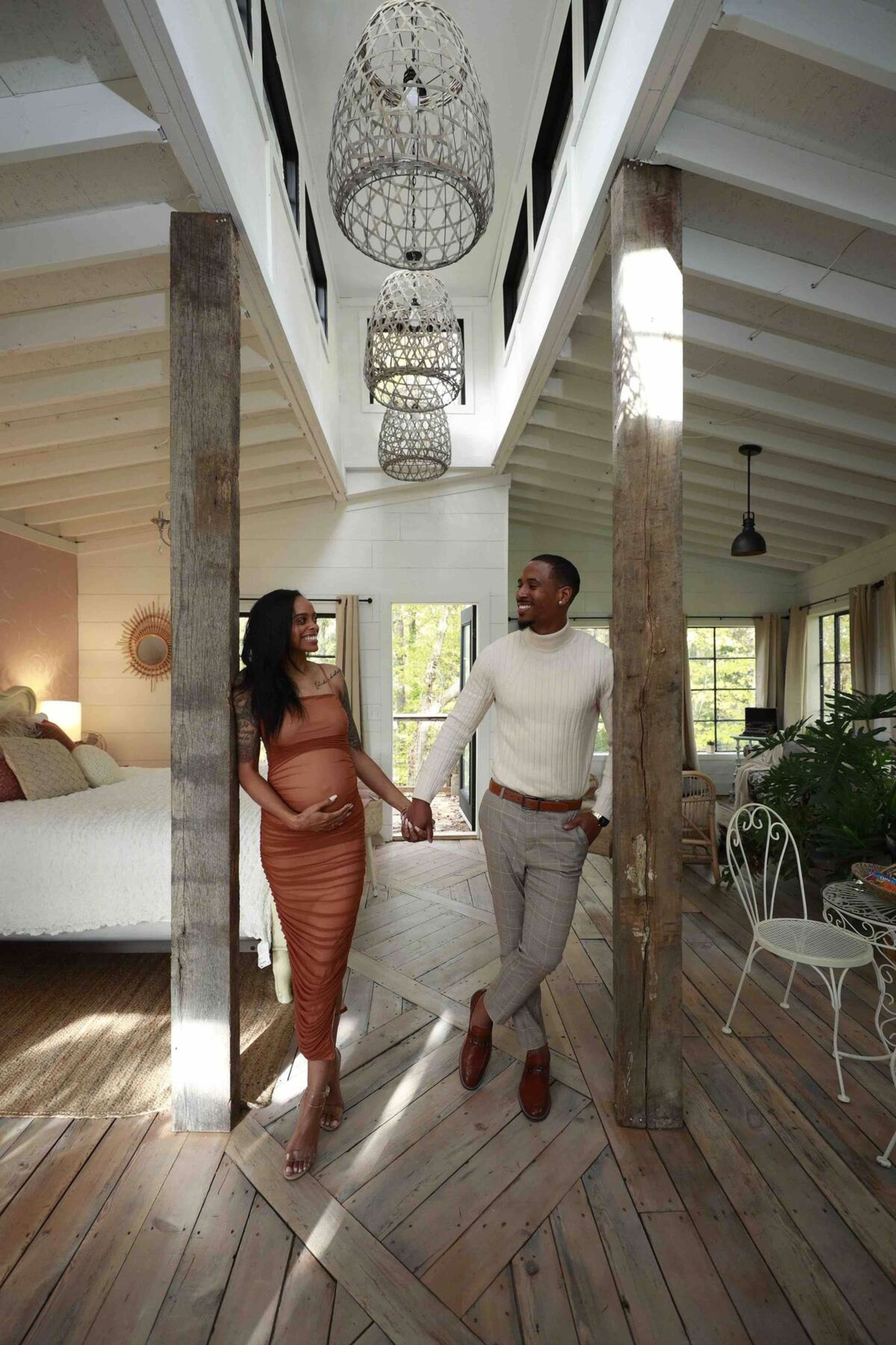 A couple holds hands and walks together in a well-lit modern interior featuring wooden beams and intricate light fixtures.