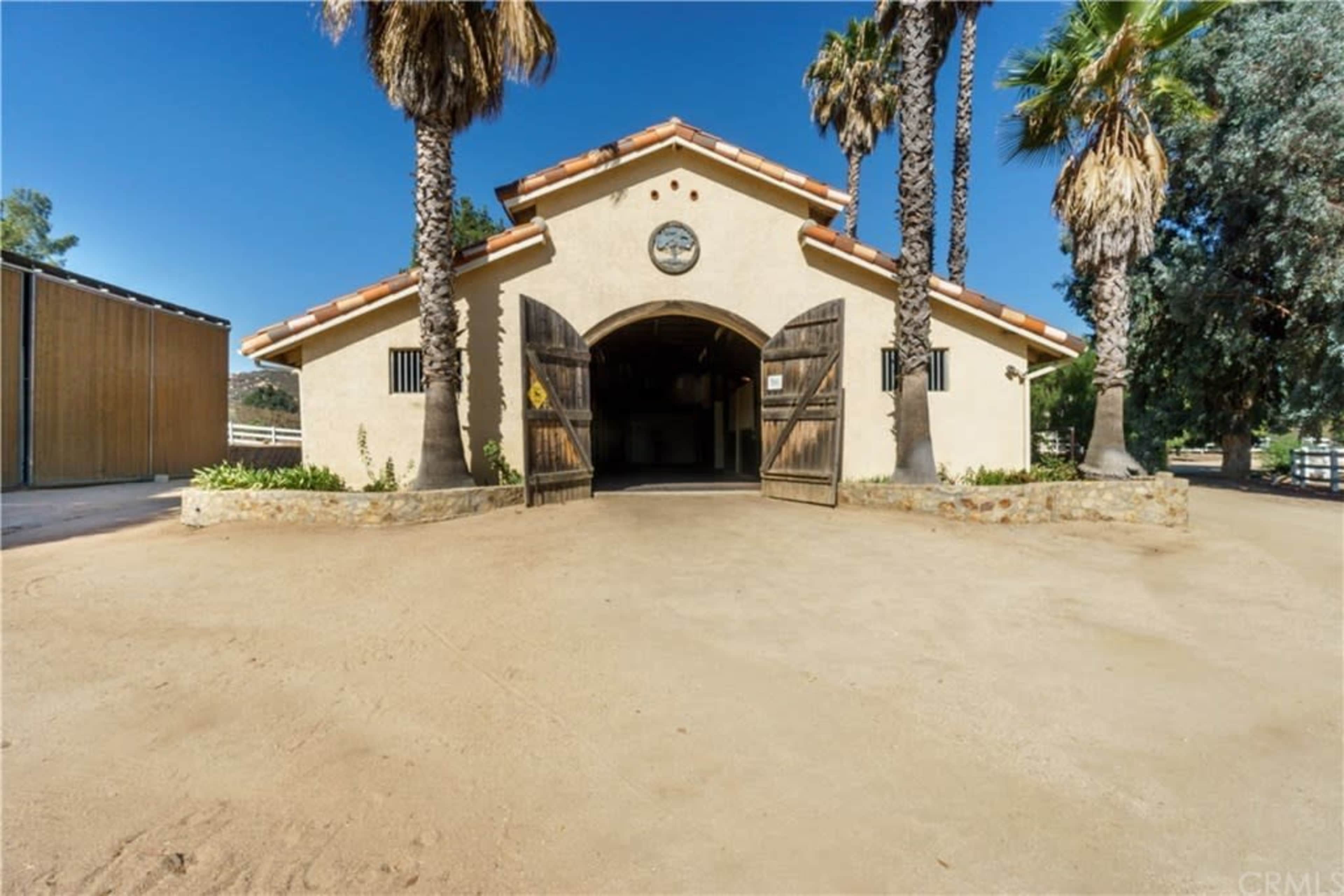 A large barn with open wooden doors and palm trees in the surrounding area.
