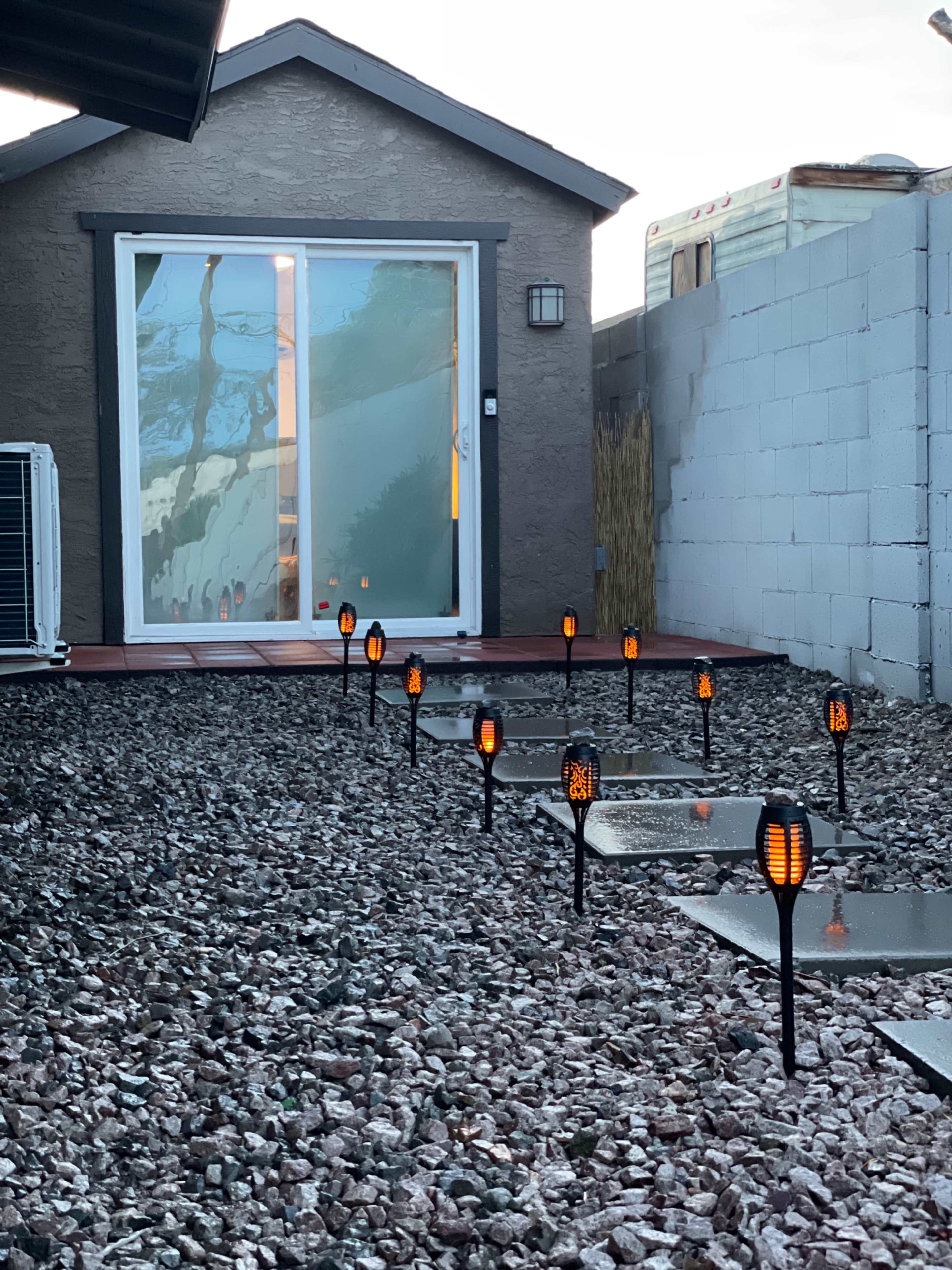 A pathway lined with solar-powered lights leads to a house with large glass doors and a gravel yard.