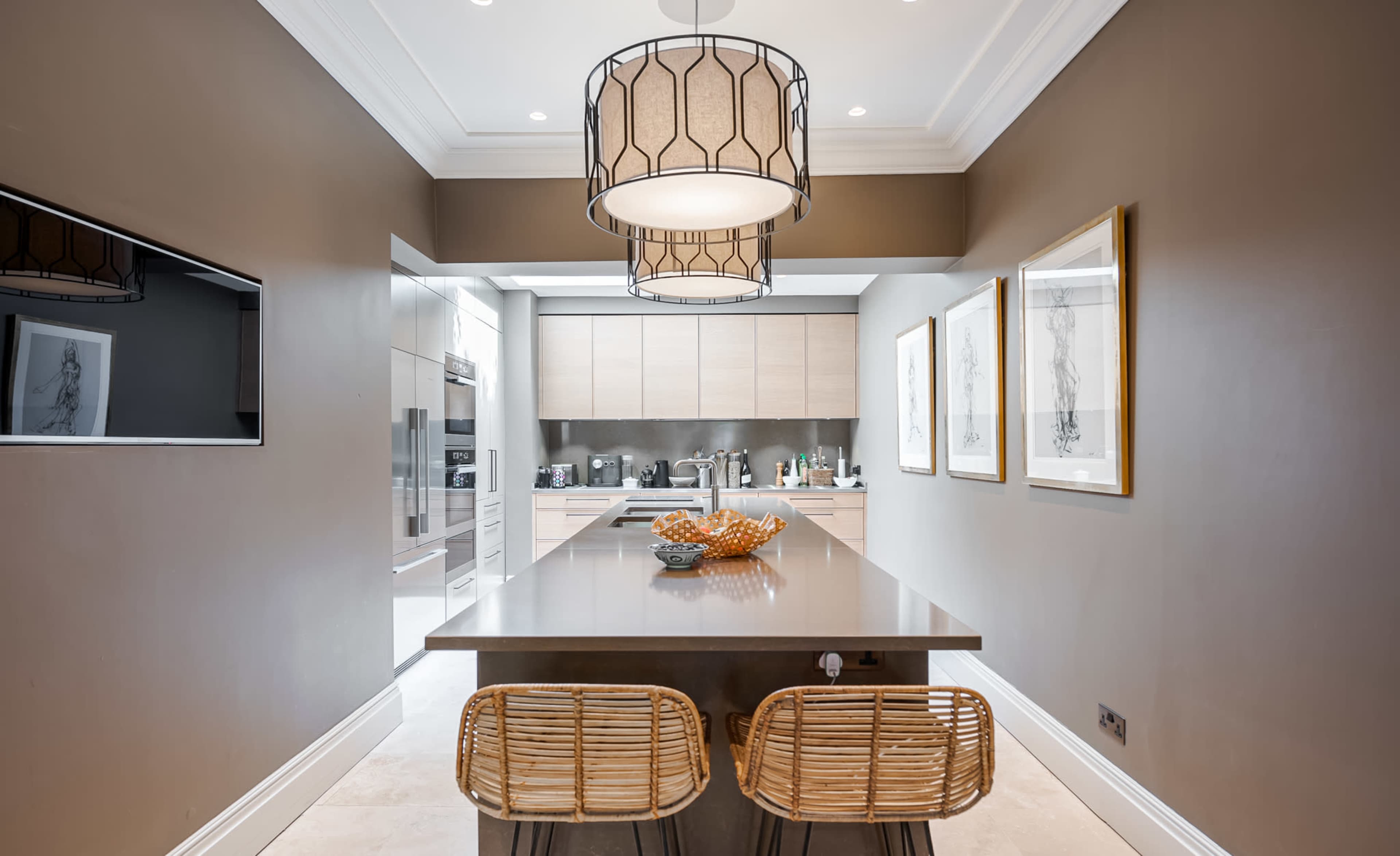A modern kitchen with light wood cabinets, a large central island, and two rattan stools.