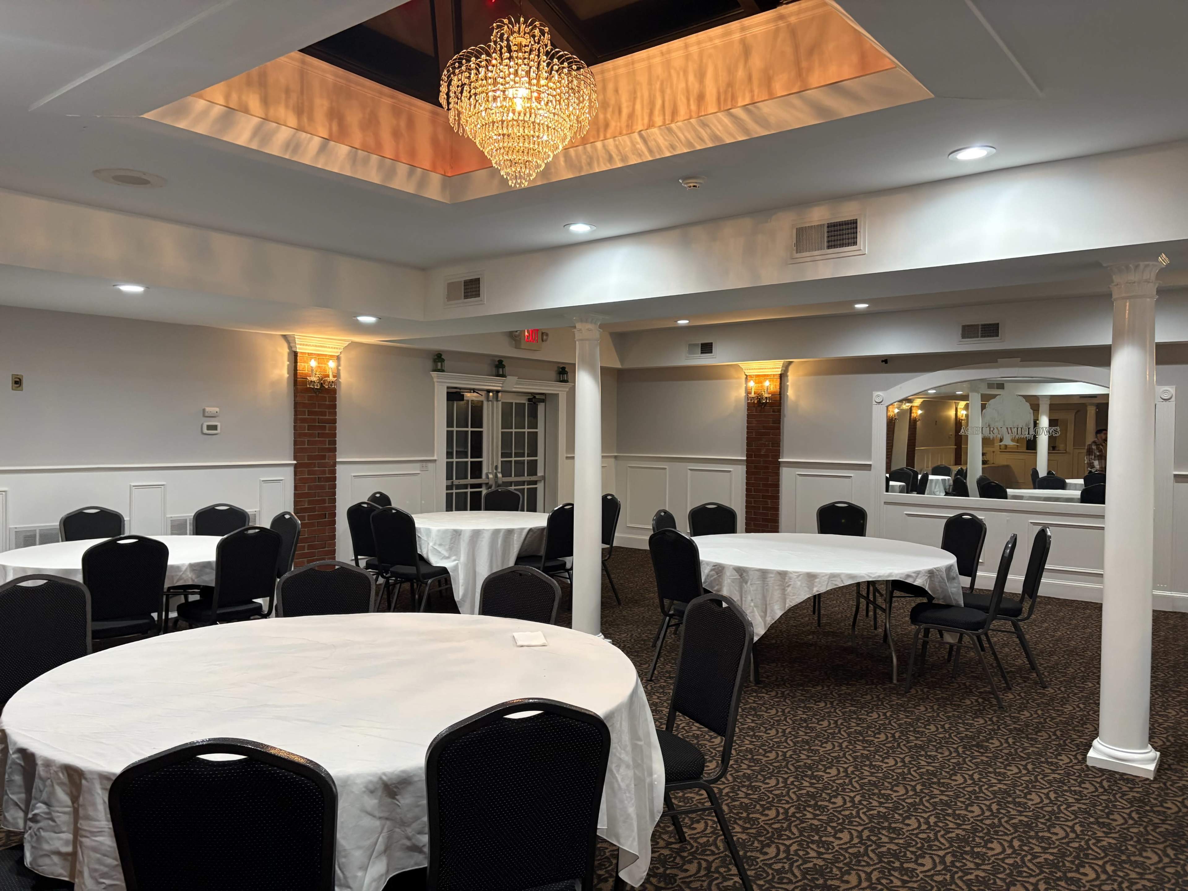The image shows a banquet hall with round tables covered in white tablecloths and a chandelier hanging from the ceiling.