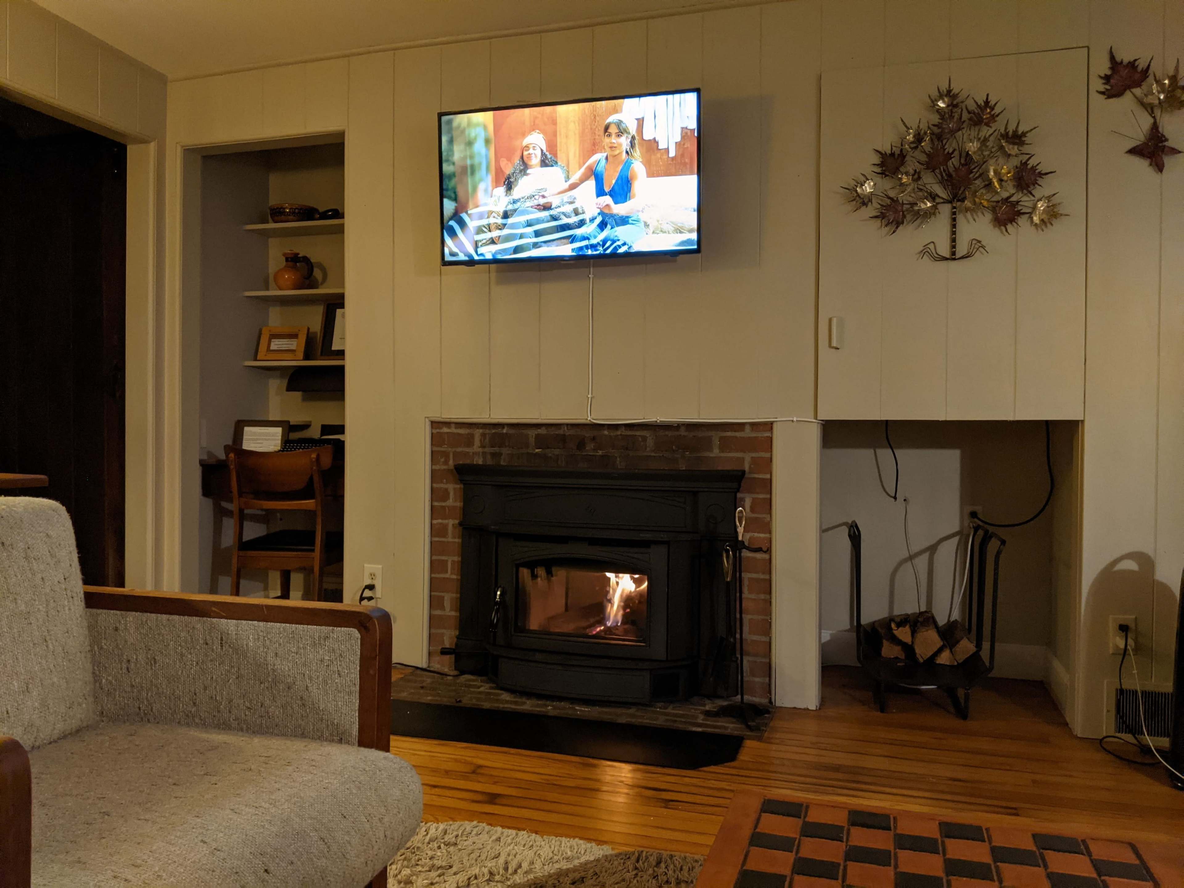 A cozy living room features a fireplace, a television mounted on the wall, and a seating area with a small wooden table.