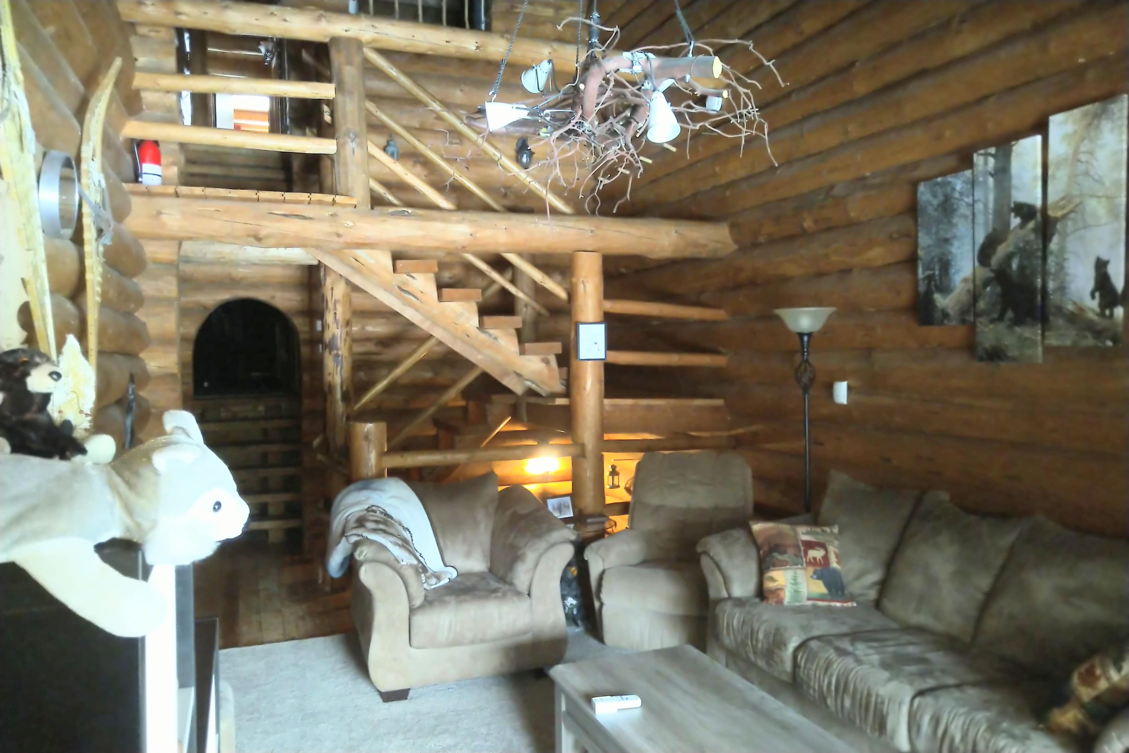 A cabin interior featuring wooden walls, a staircase, a cozy seating area with a sofa and armchair, and decorative wall art.
