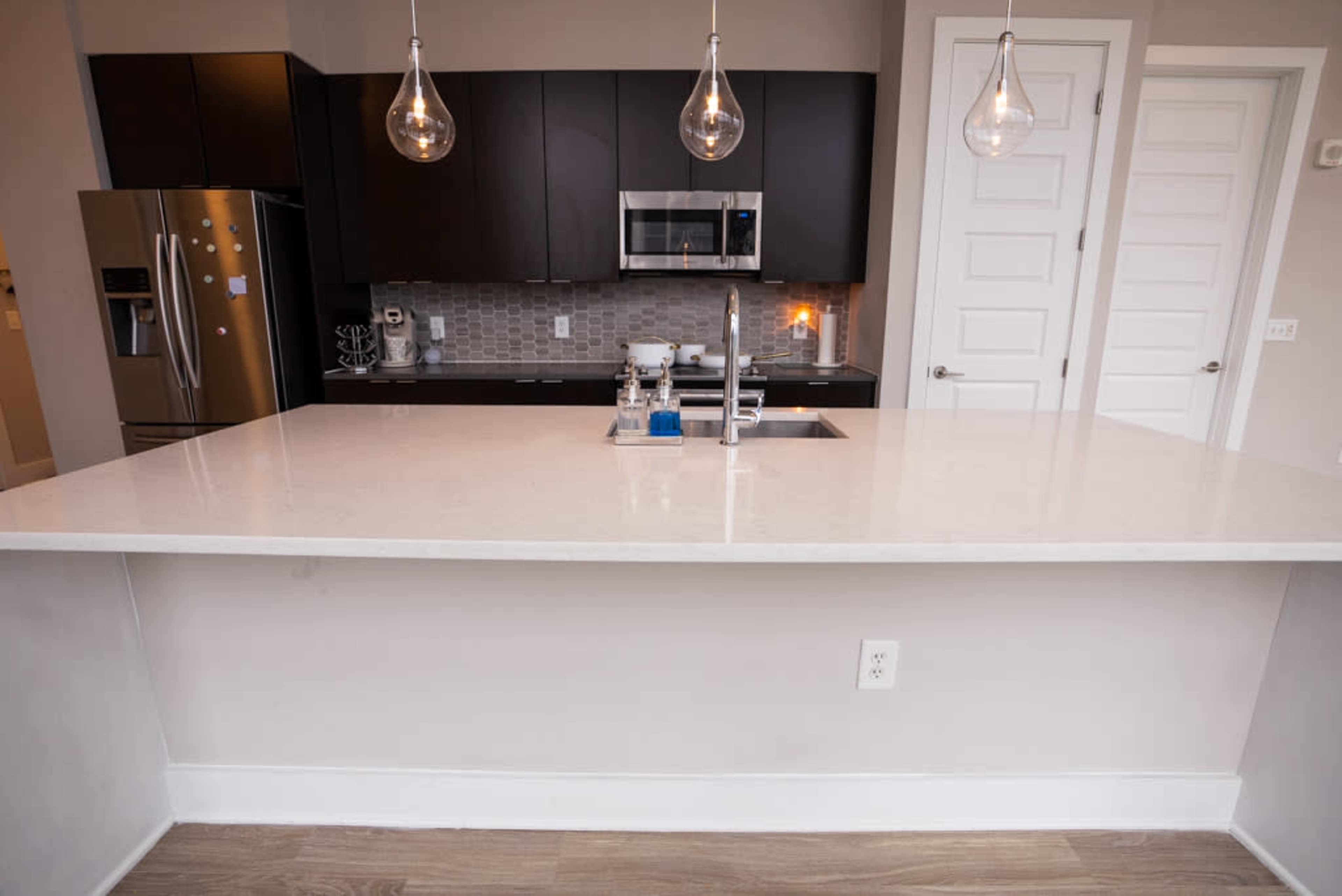 The image shows a modern kitchen with a light-colored countertop, black cabinets, and pendant lighting above the island.
