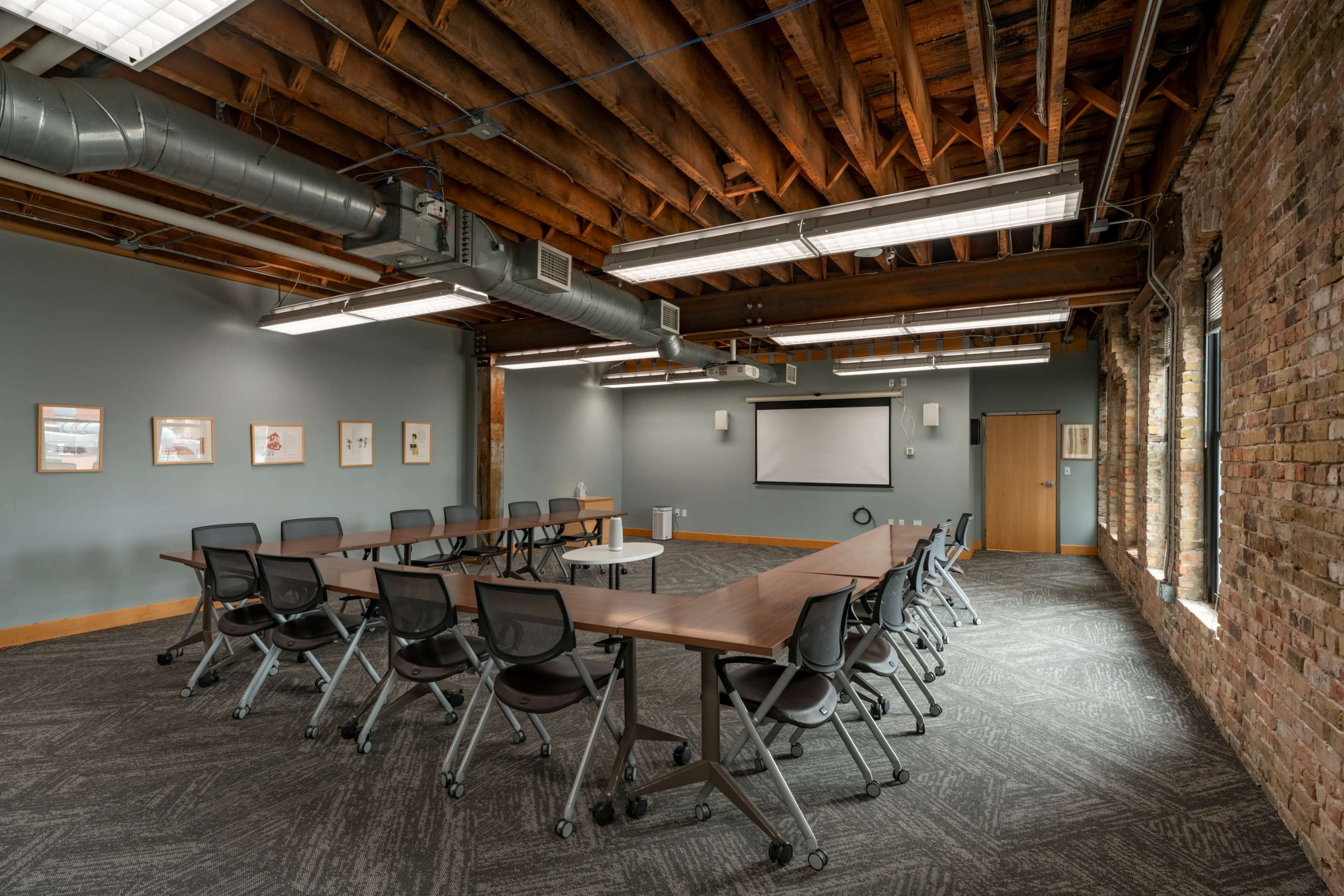 A spacious conference room features a large, rectangular table surrounded by rolling chairs, with exposed wooden beams and brick walls.