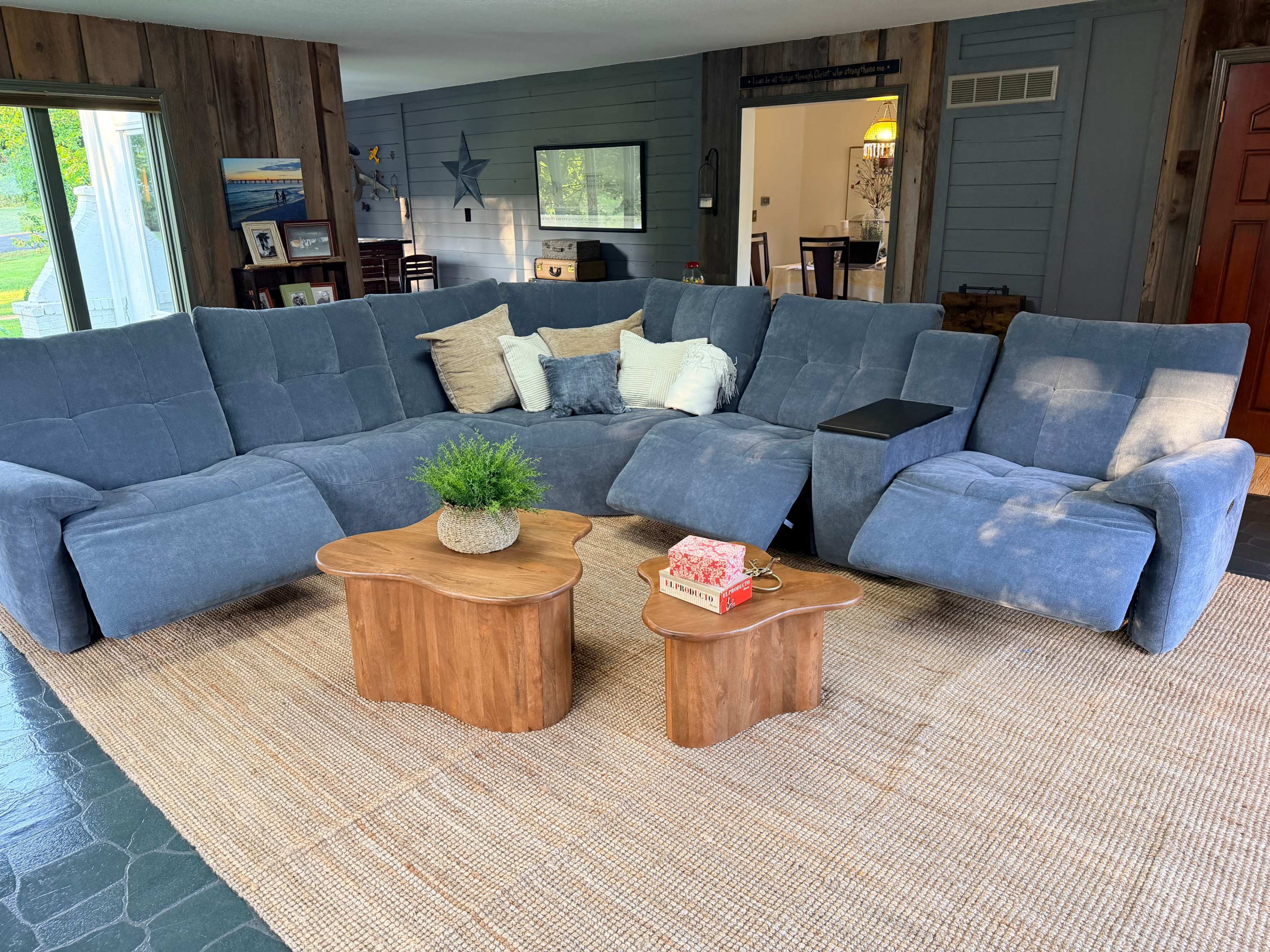 The image shows a modern sectional sofa arranged in a living room with wooden walls and two coffee tables in front.