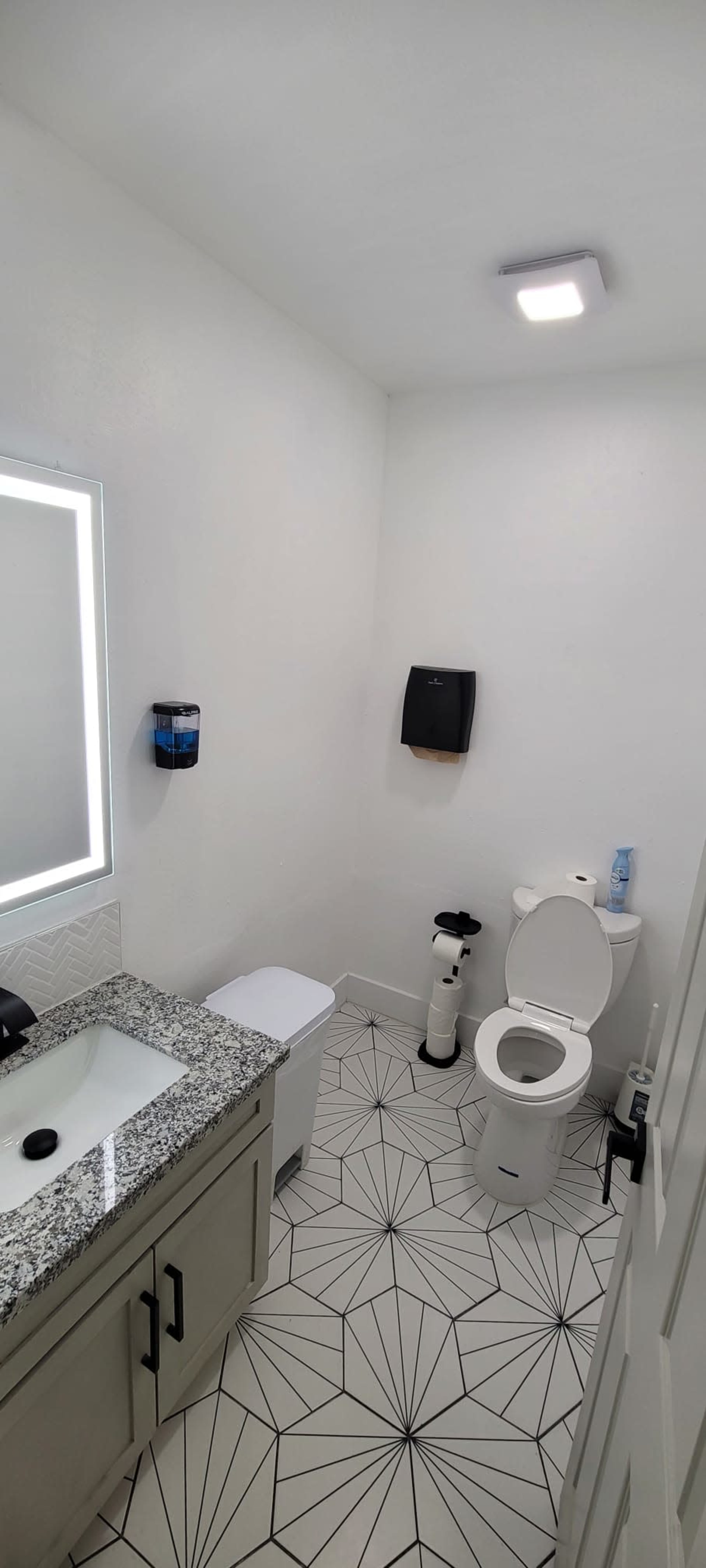 A modern bathroom featuring a toilet, a sink with a granite countertop, and geometric patterned floor tiles.