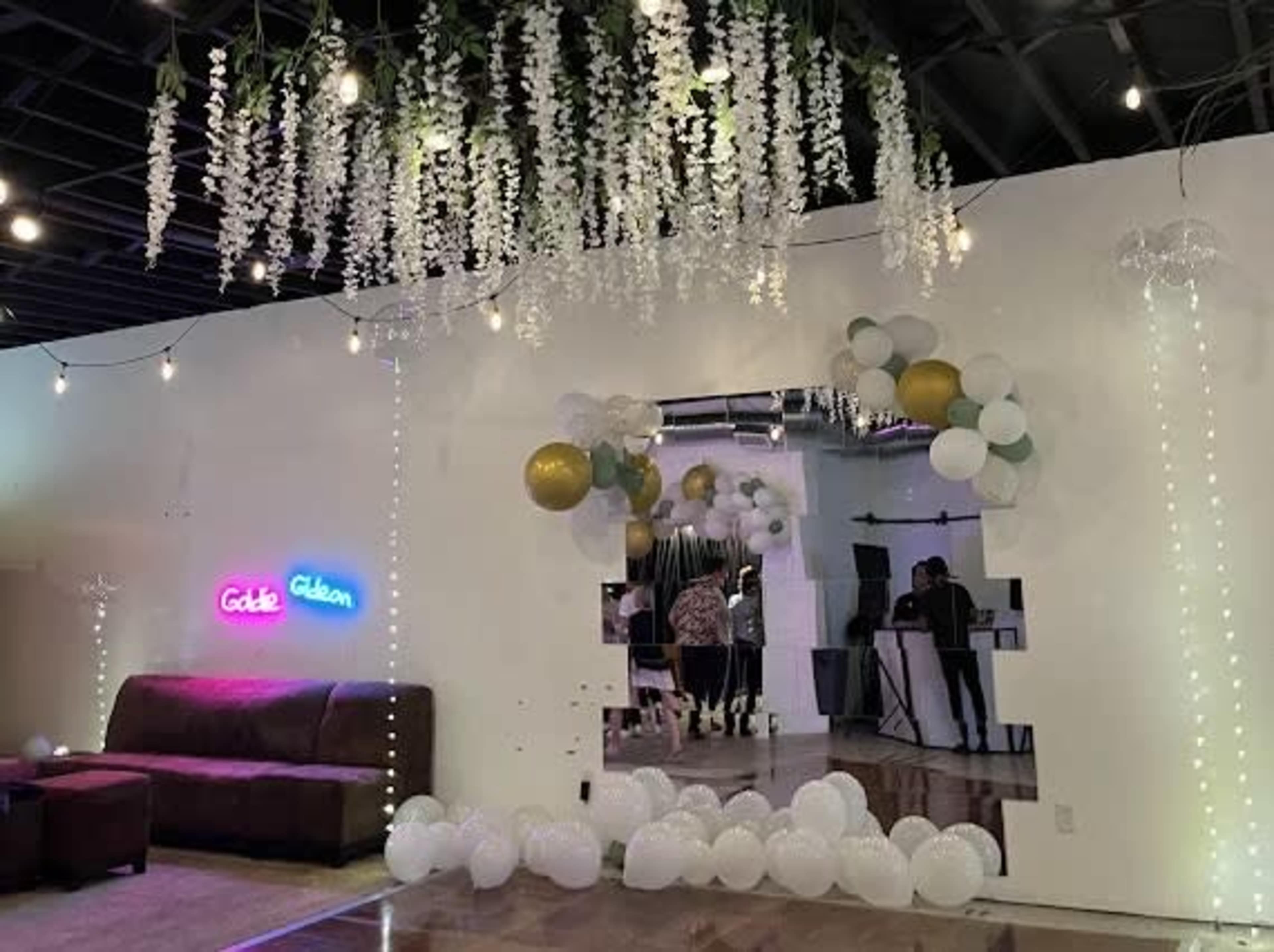 A decorated event space with a mirrored wall feature, balloons, string lights, and a neon sign reading "Gold & Gibbon."