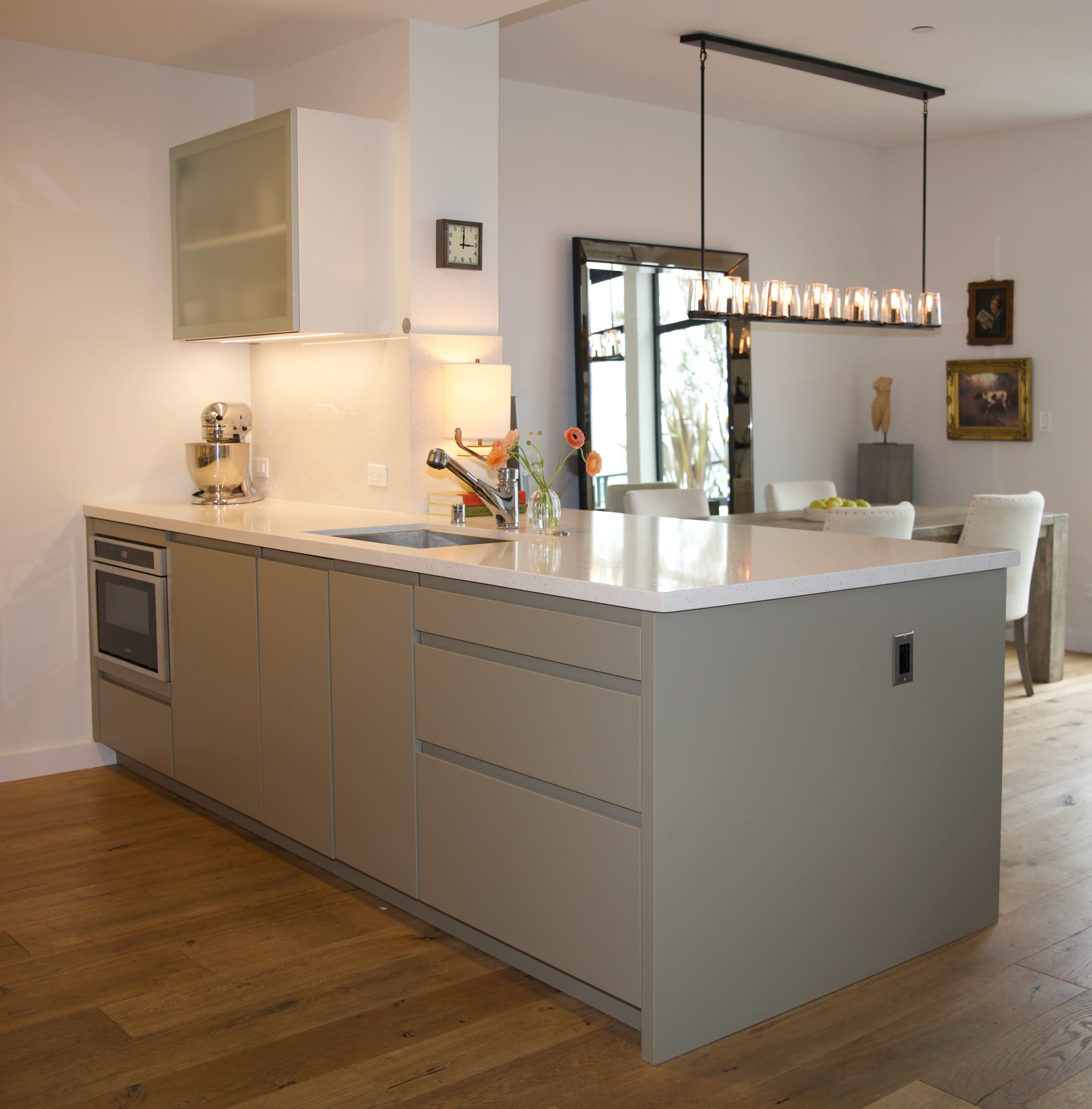 A modern kitchen with an island featuring a sink, sleek cabinetry, and a dining area visible in the background.