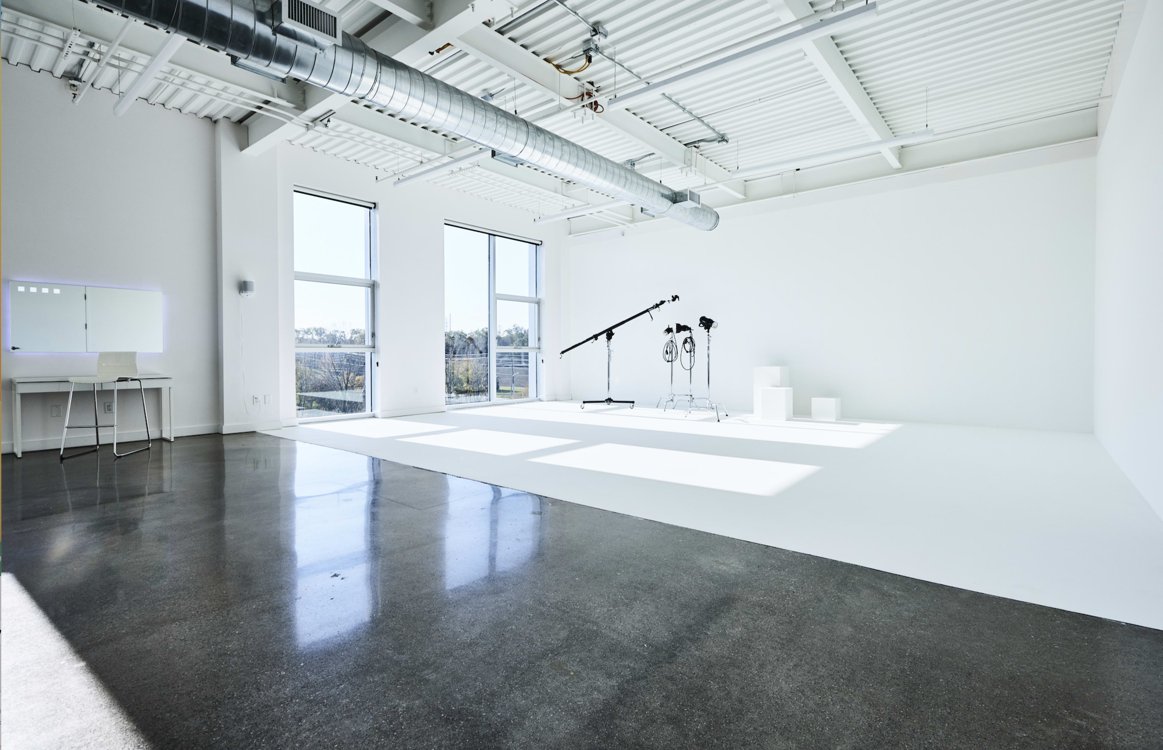 A spacious, well-lit studio with large windows, polished concrete flooring, and photography equipment set up against a white backdrop.