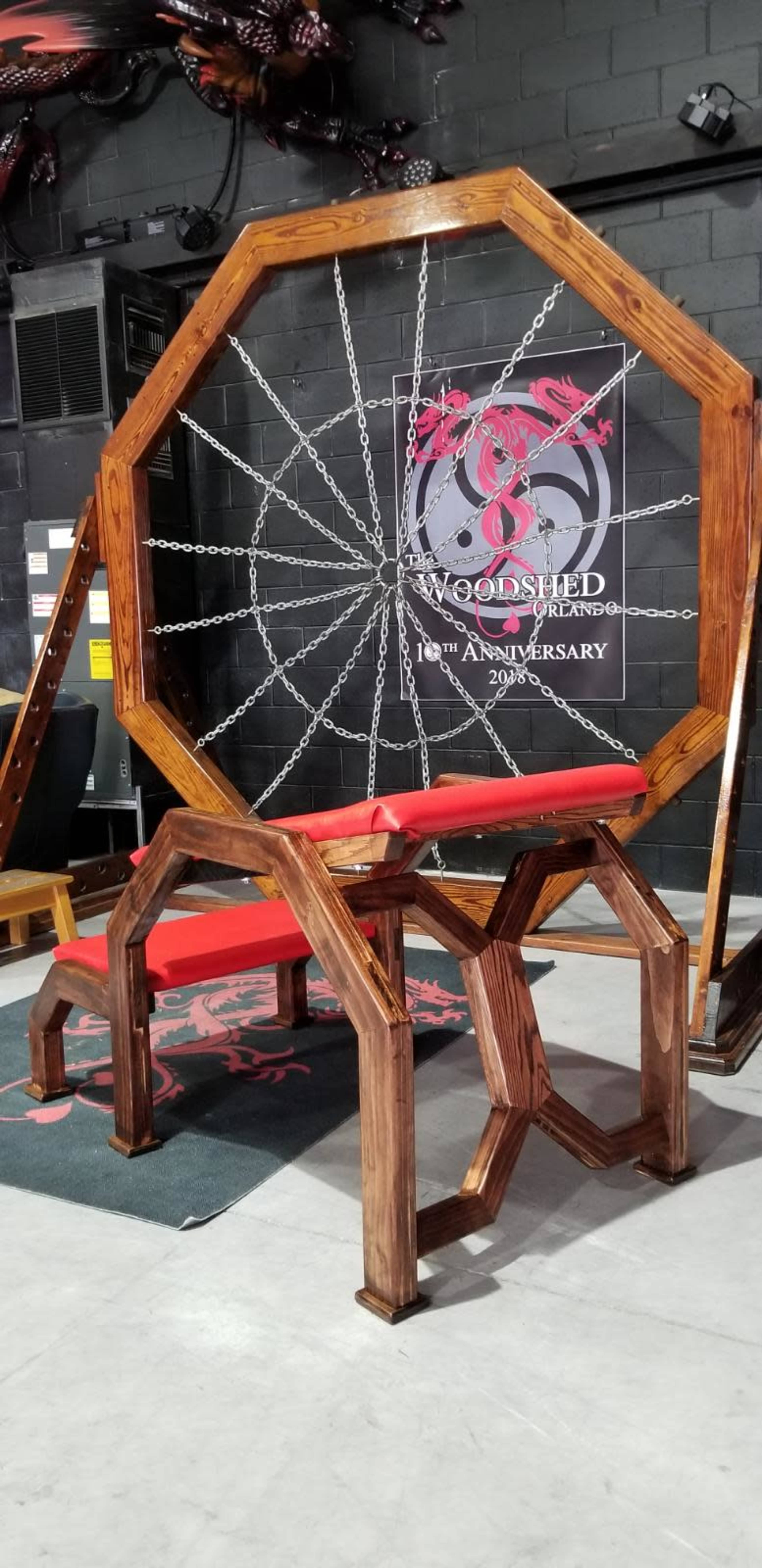 A wooden octagonal frame with chains attached, placed in front of a backdrop featuring a logo for the "Woolshed" and its anniversary.