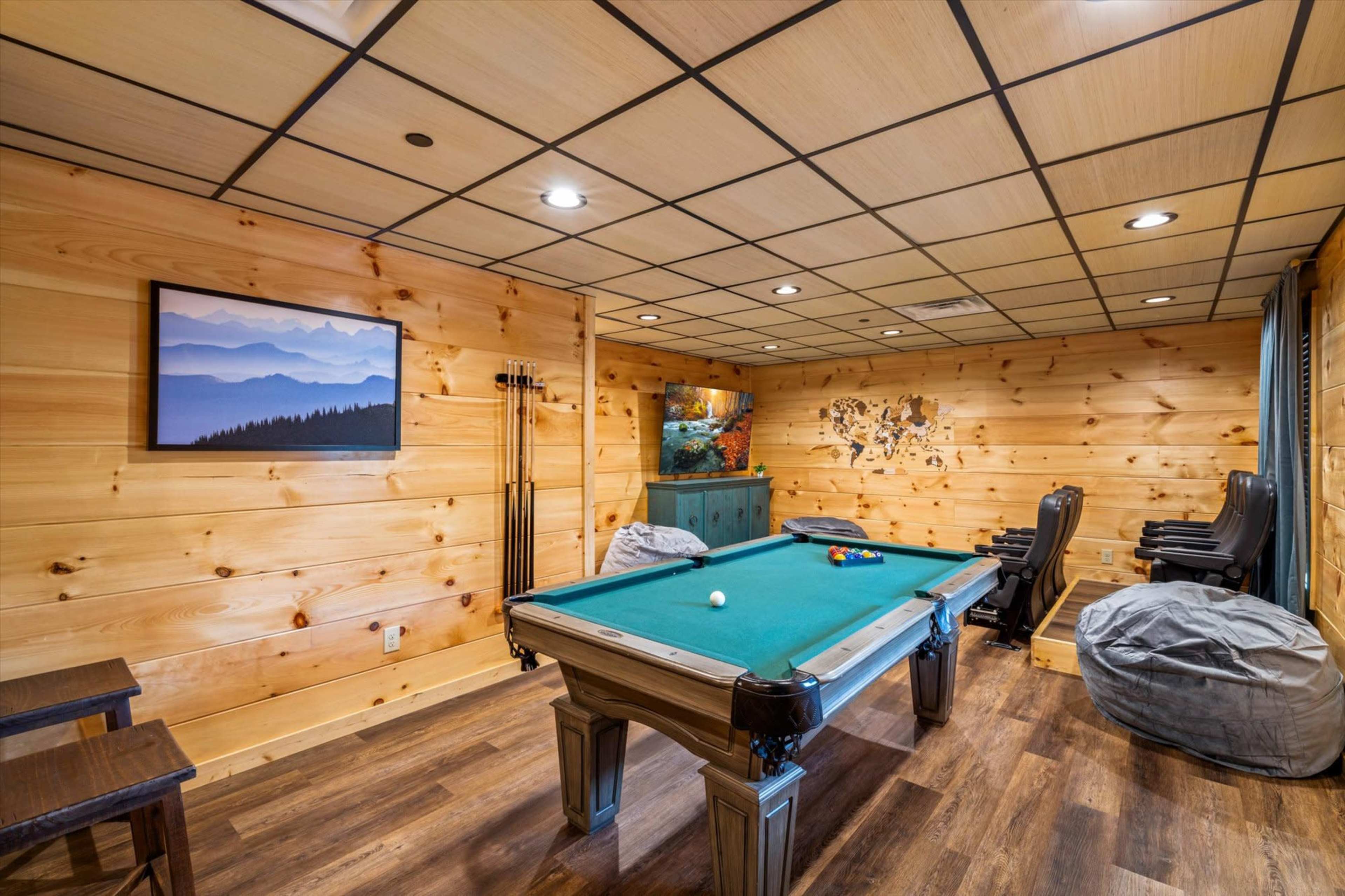 A game room featuring a pool table, wooden paneling, and bean bag chairs against a backdrop of mountain-themed artwork.