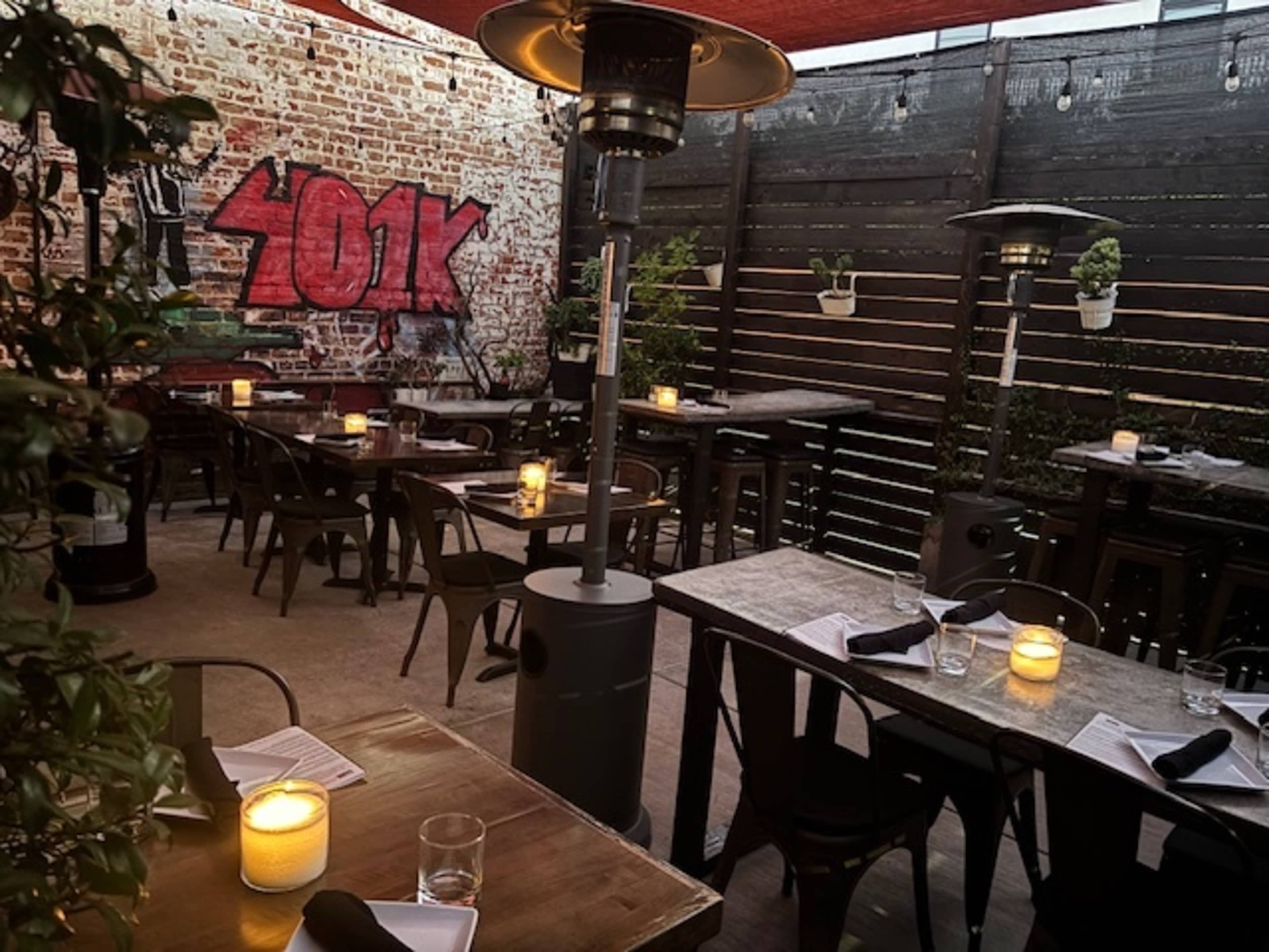 The image shows an outdoor restaurant patio with tables set up, glowing candles on each table, and a graffiti mural on a brick wall.