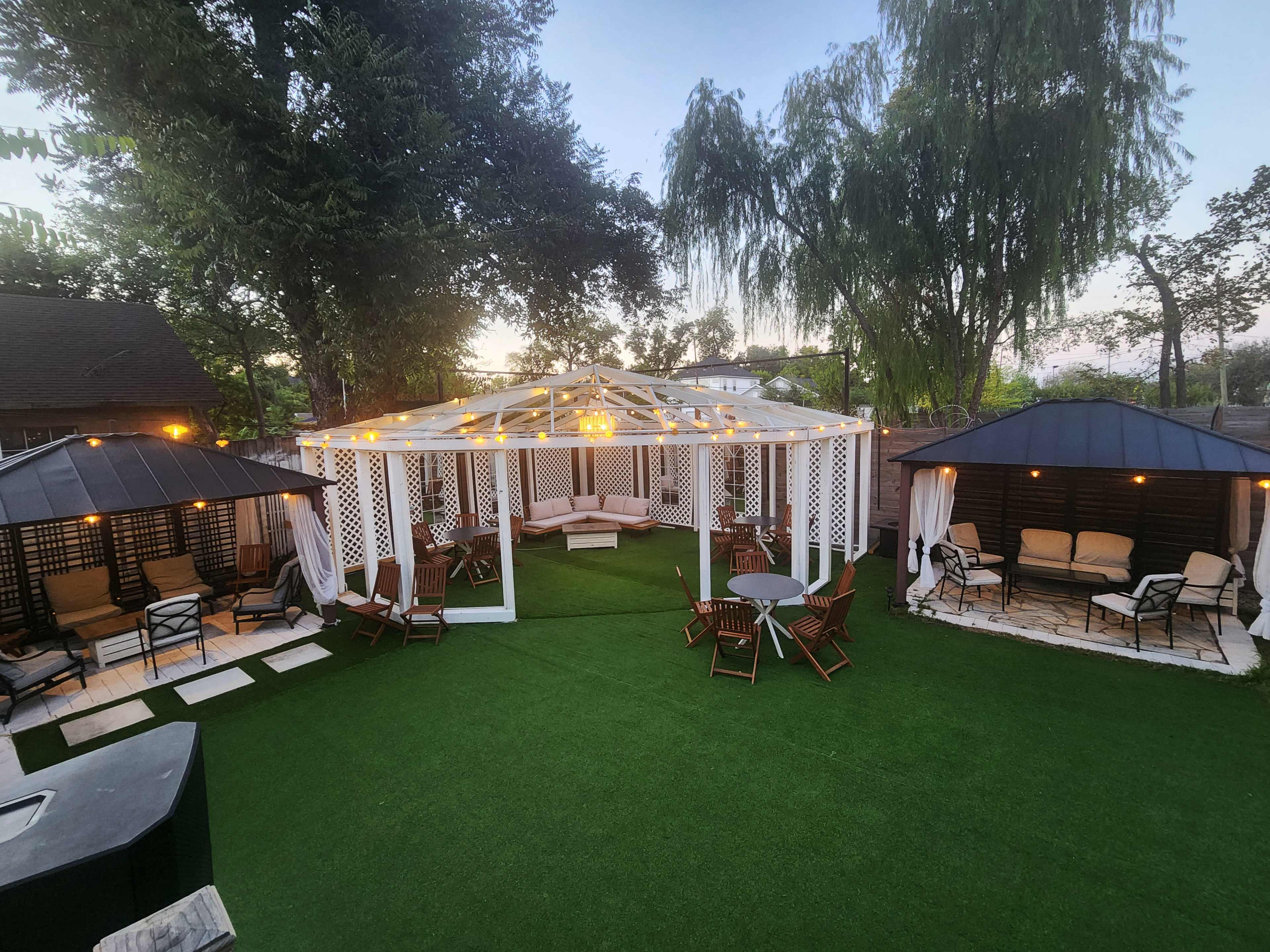 The image shows a landscaped outdoor area featuring a gazebo surrounded by seating arrangements, artificial grass, and two patio structures.