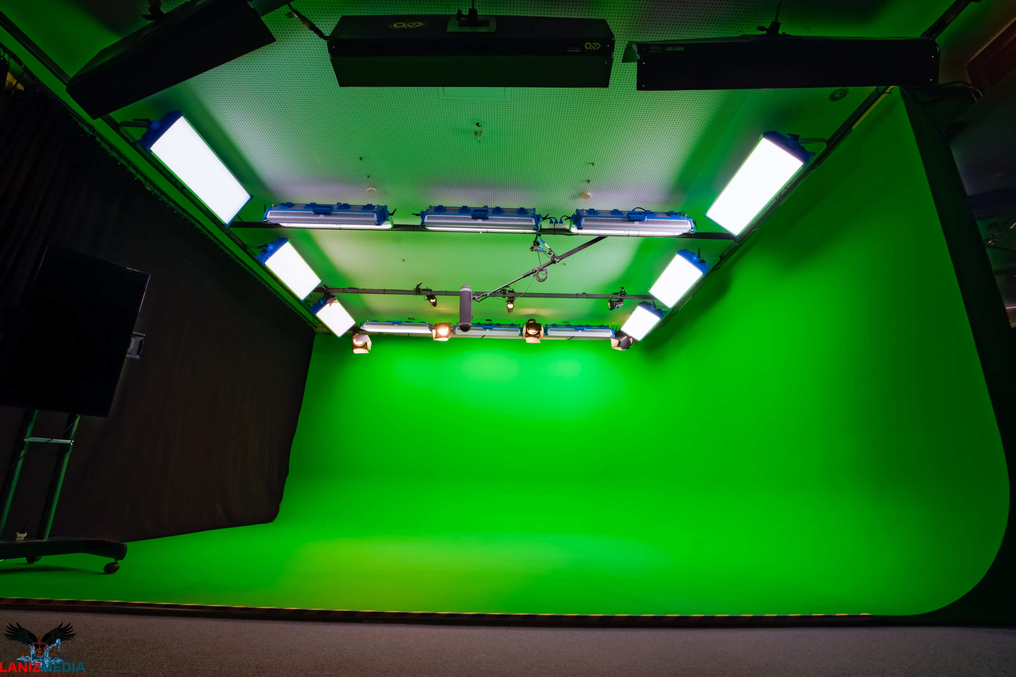 The image shows a green screen studio with bright overhead lights and a dark curtain on one side.