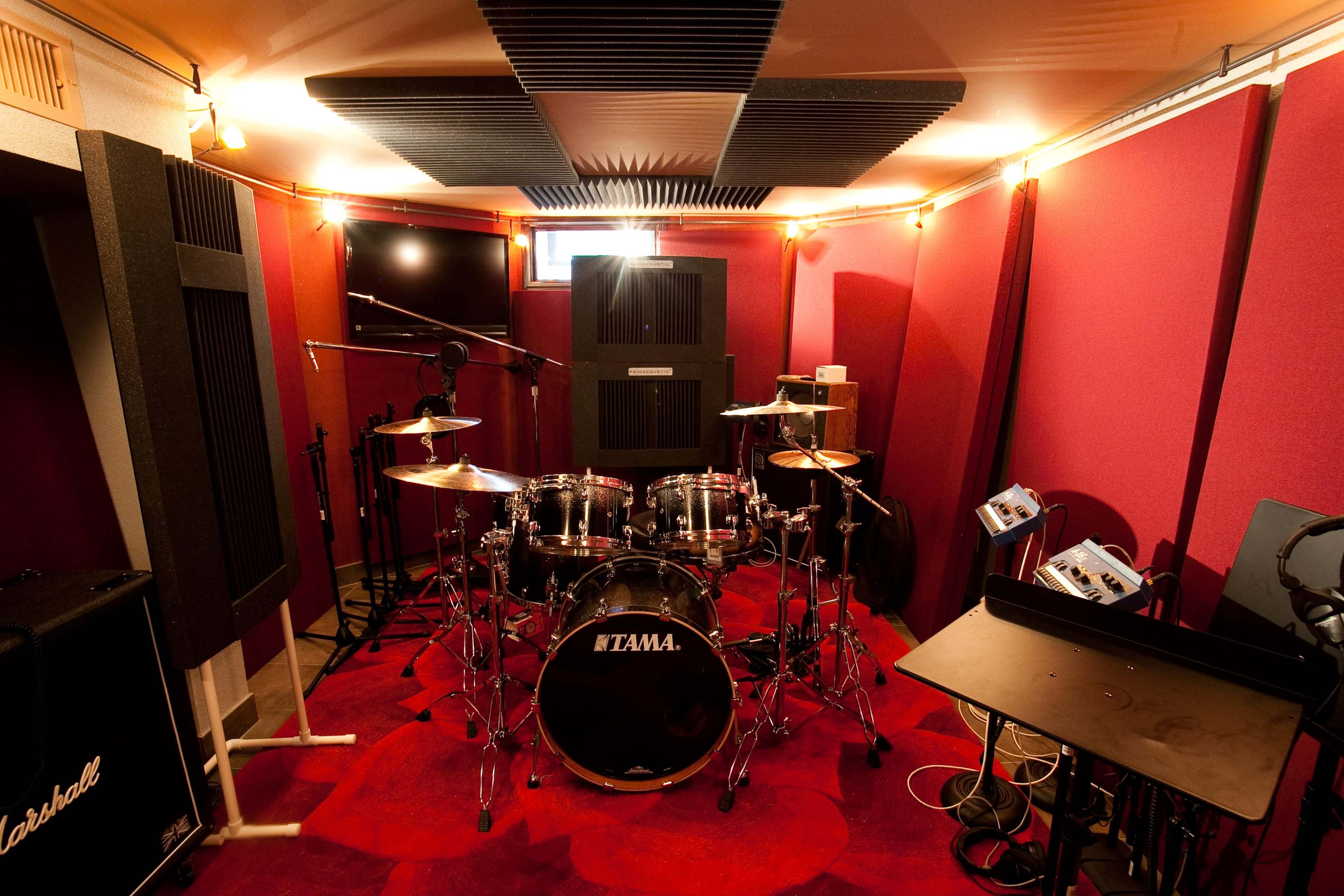 A soundproof music studio equipped with a drum set, amplifiers, and sound-absorbing panels on the walls.