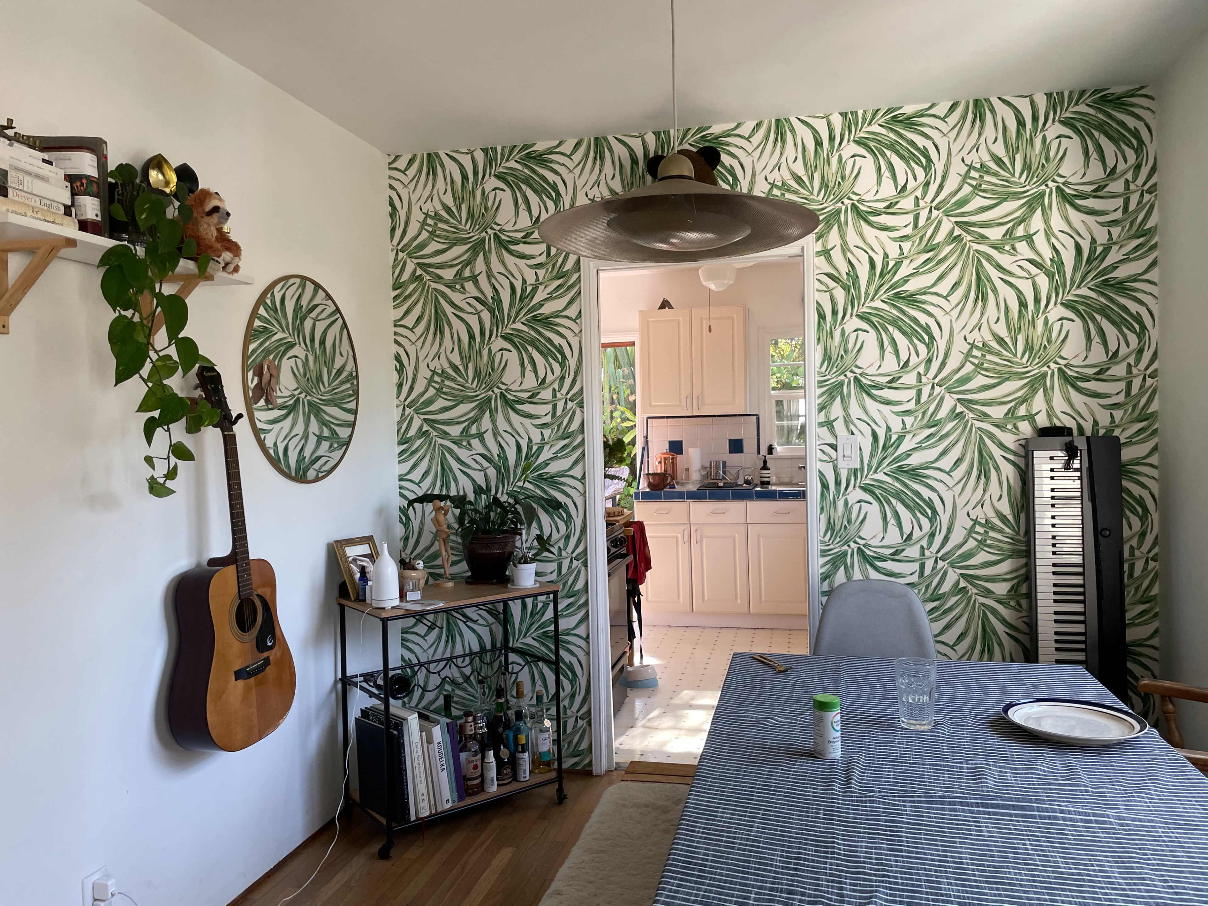 A dining area features a table with a striped tablecloth, surrounded by chairs, and a wall adorned with green leaf-patterned wallpaper.