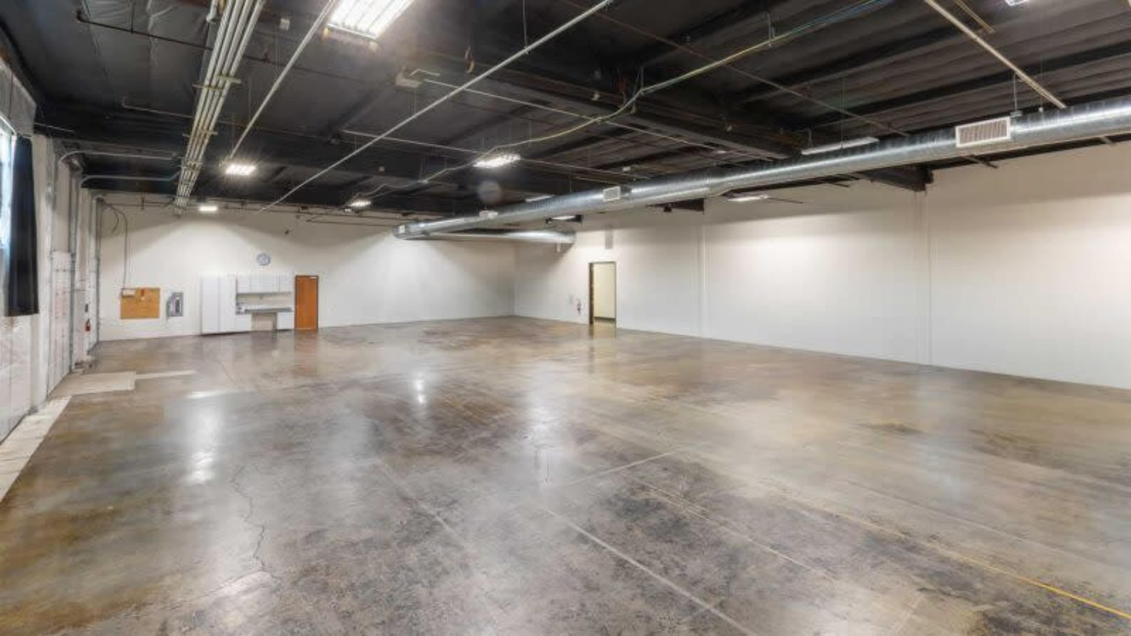 A large, empty industrial space with a polished concrete floor and exposed ceiling fixtures.