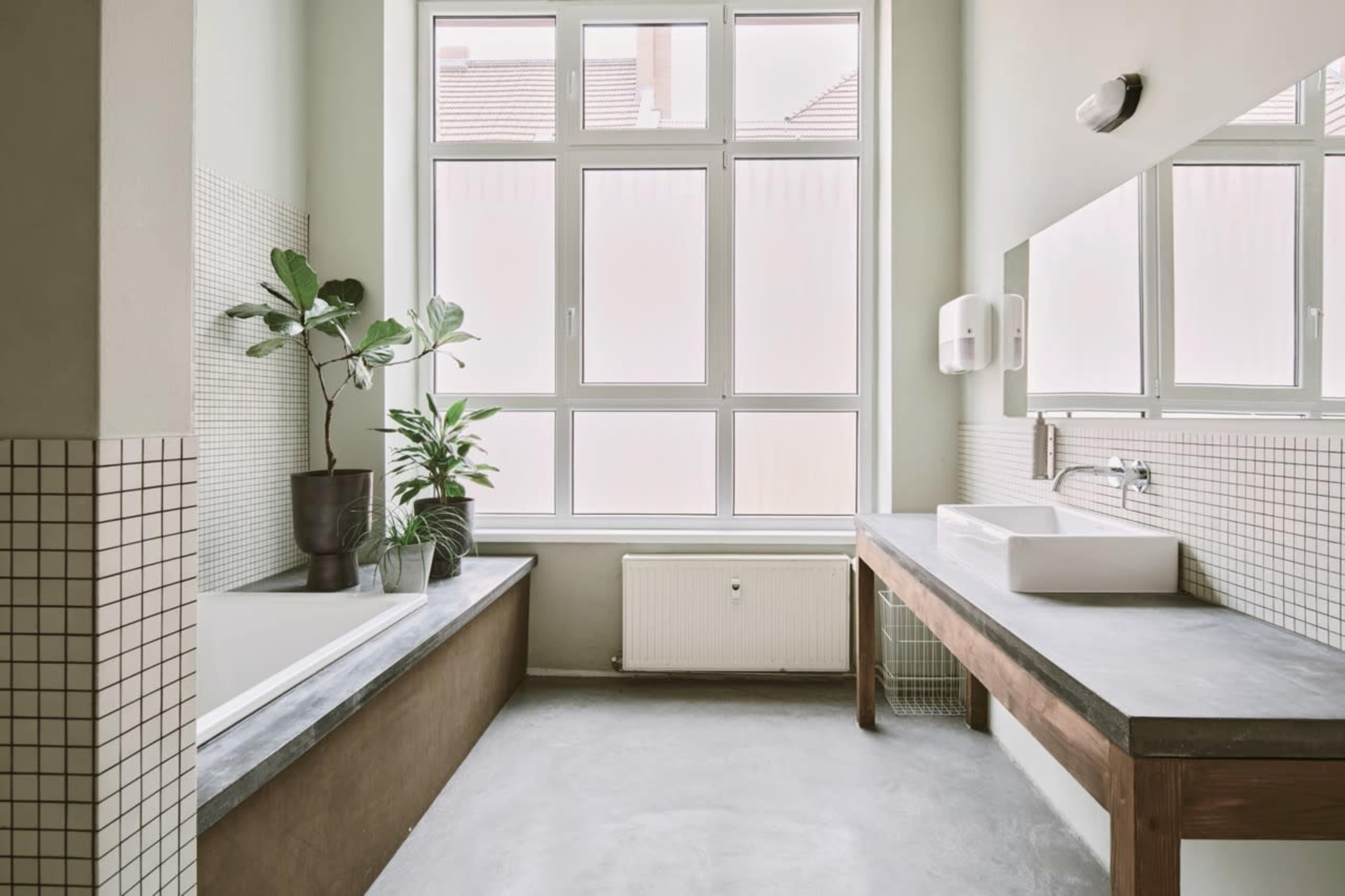 A modern bathroom features a large window, a freestanding tub with plants nearby, and a wooden vanity with a sink.