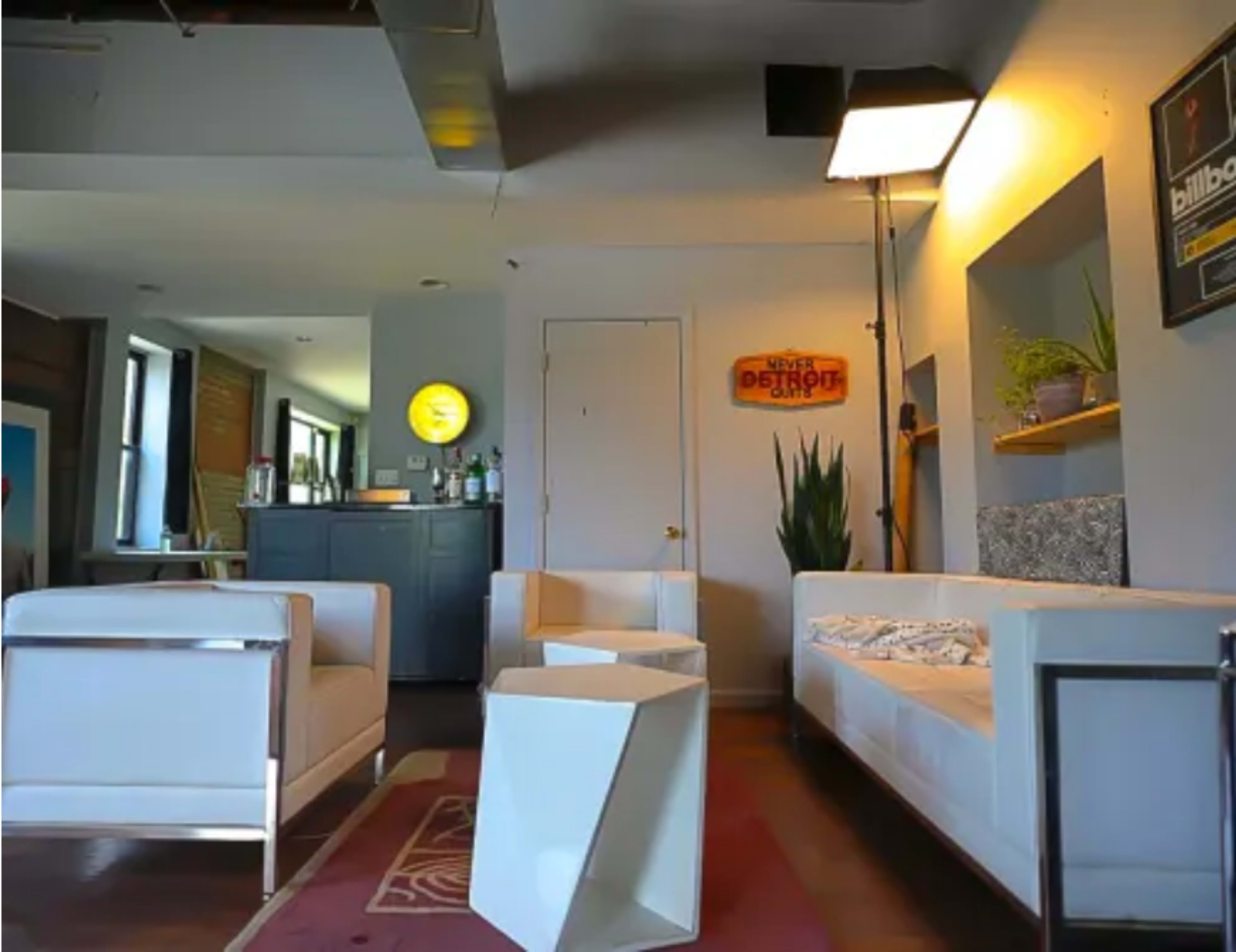 A modern lounge area with white furniture, a bar counter stocked with bottles, and a triangular coffee table.