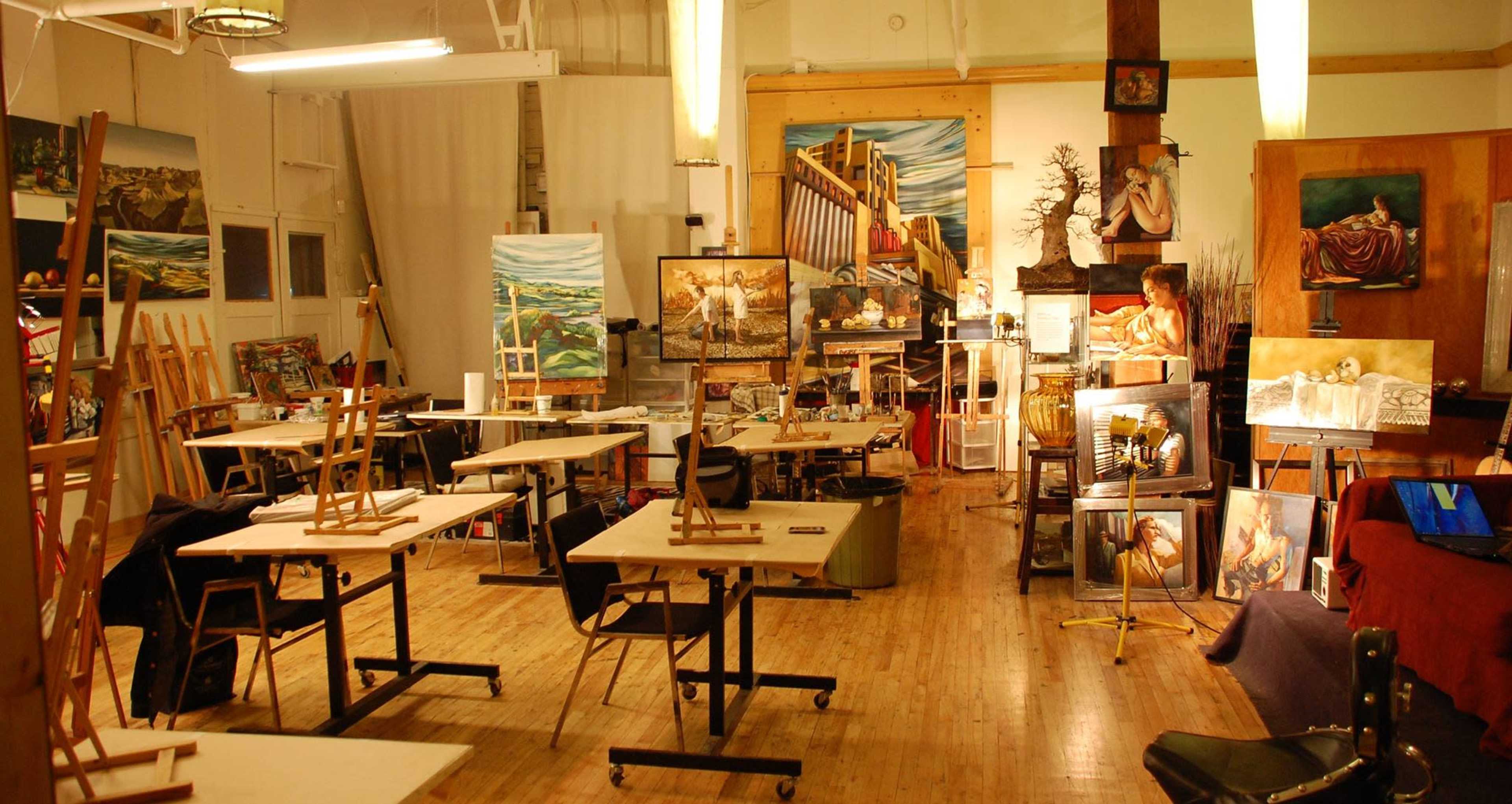An art studio filled with easels, tables, and various paintings displayed around the room.