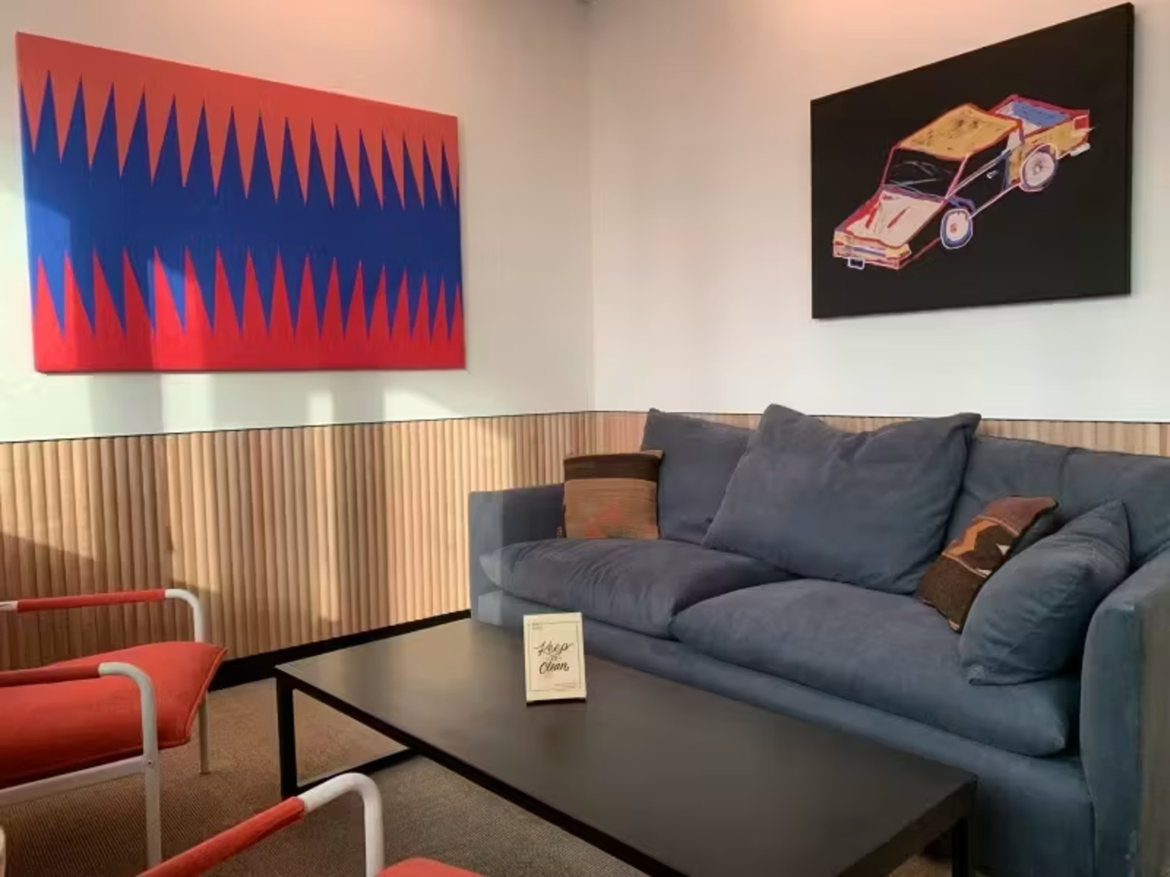 A modern interior featuring a blue sofa, a black coffee table, and colorful wall art on adjacent walls.