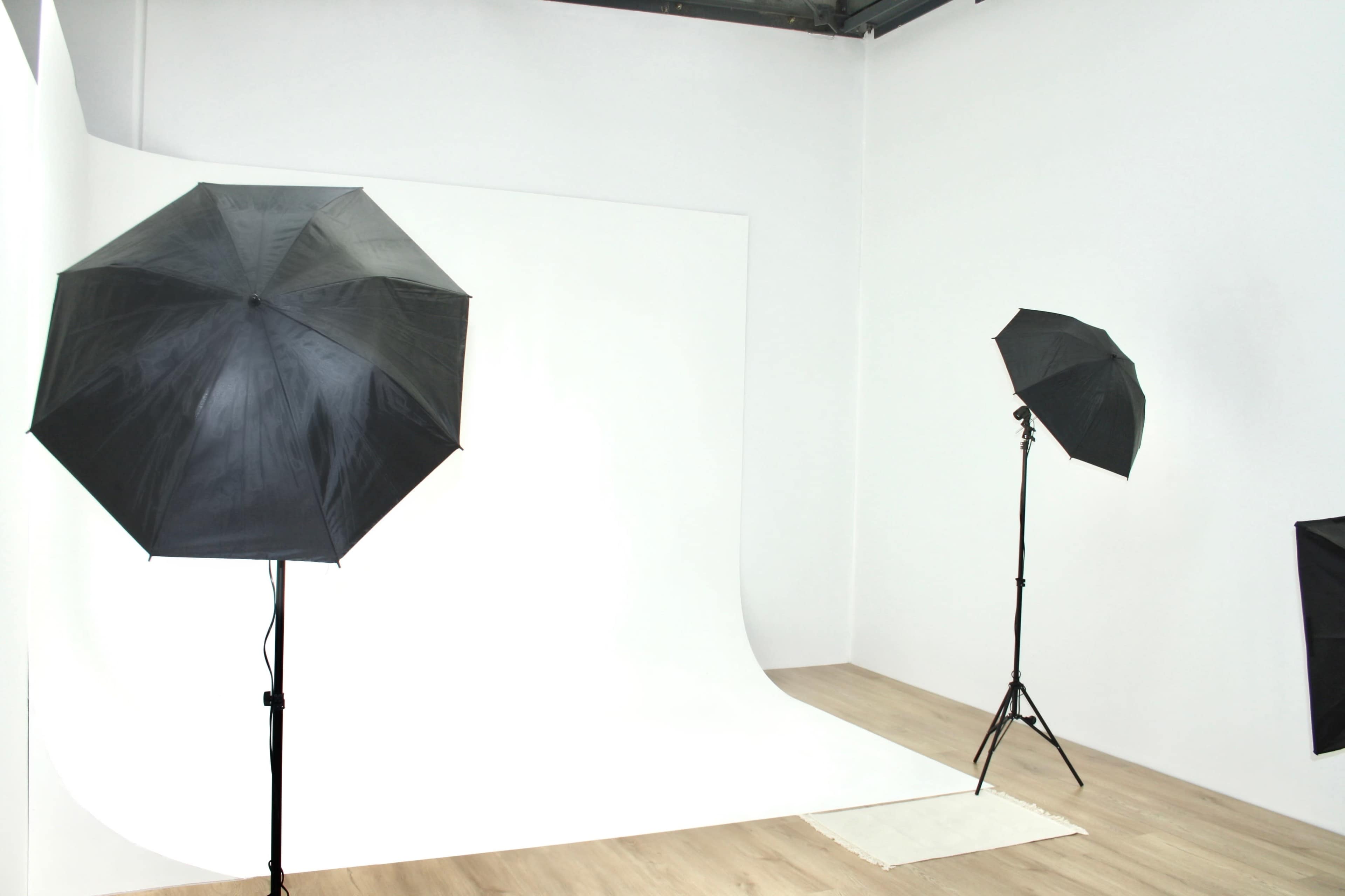 A photography studio with two black umbrellas on stands, illuminating a seamless white backdrop.