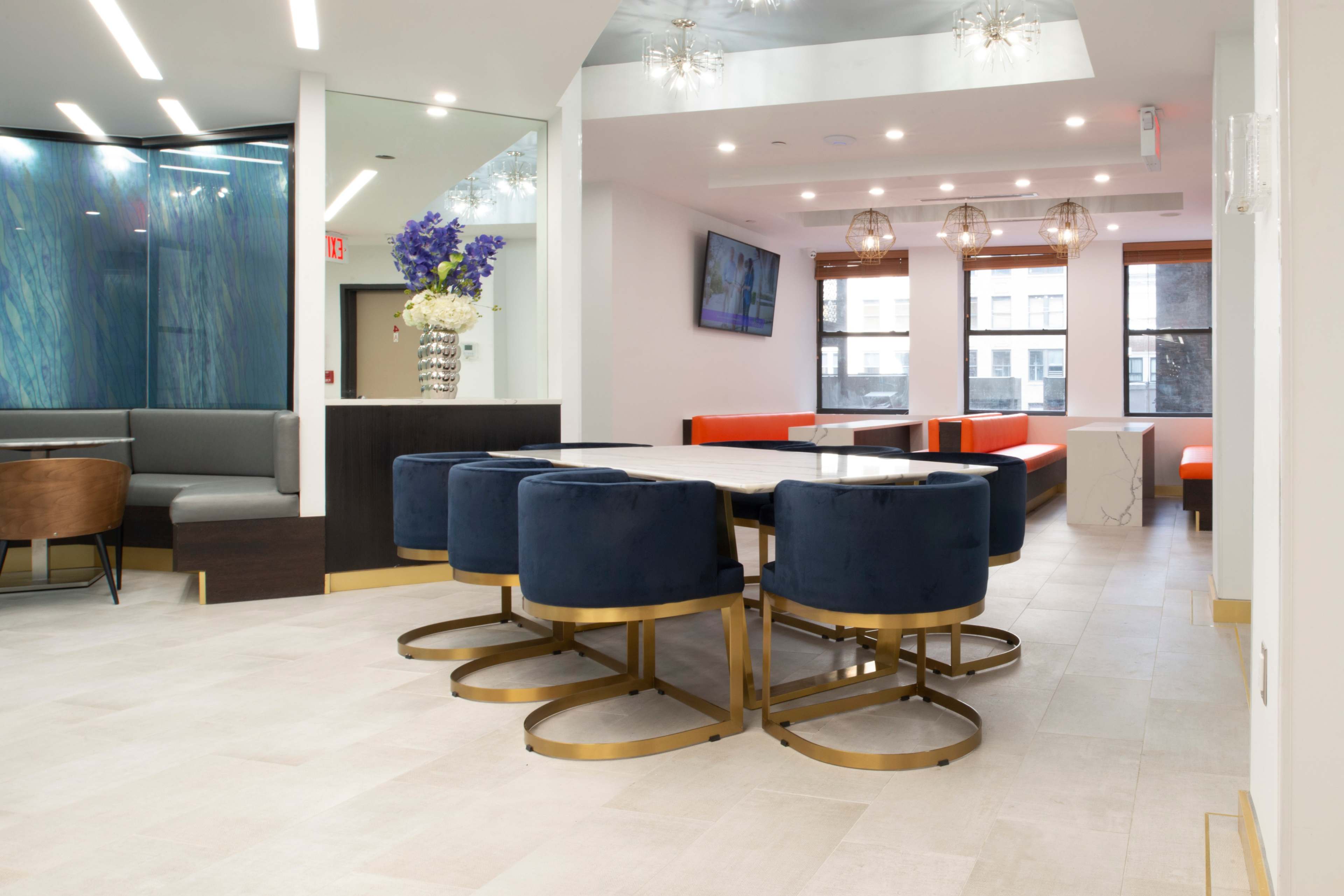 The scene shows a modern dining area featuring a round table surrounded by navy blue upholstered chairs, complemented by orange and gray seating along the walls.