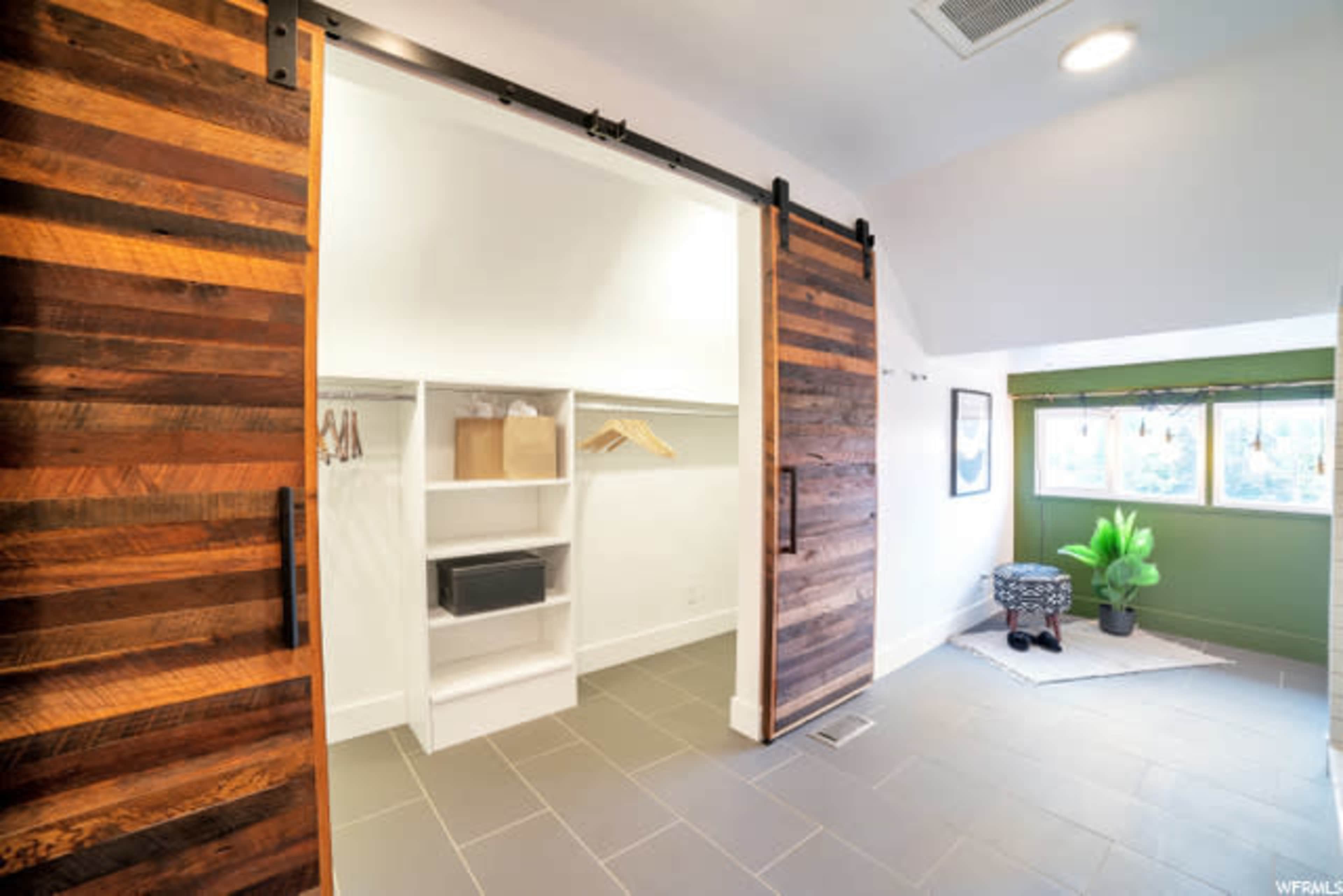 A well-lit room featuring a closet with sliding wooden doors, a shelf unit, and a small seating area near a window.