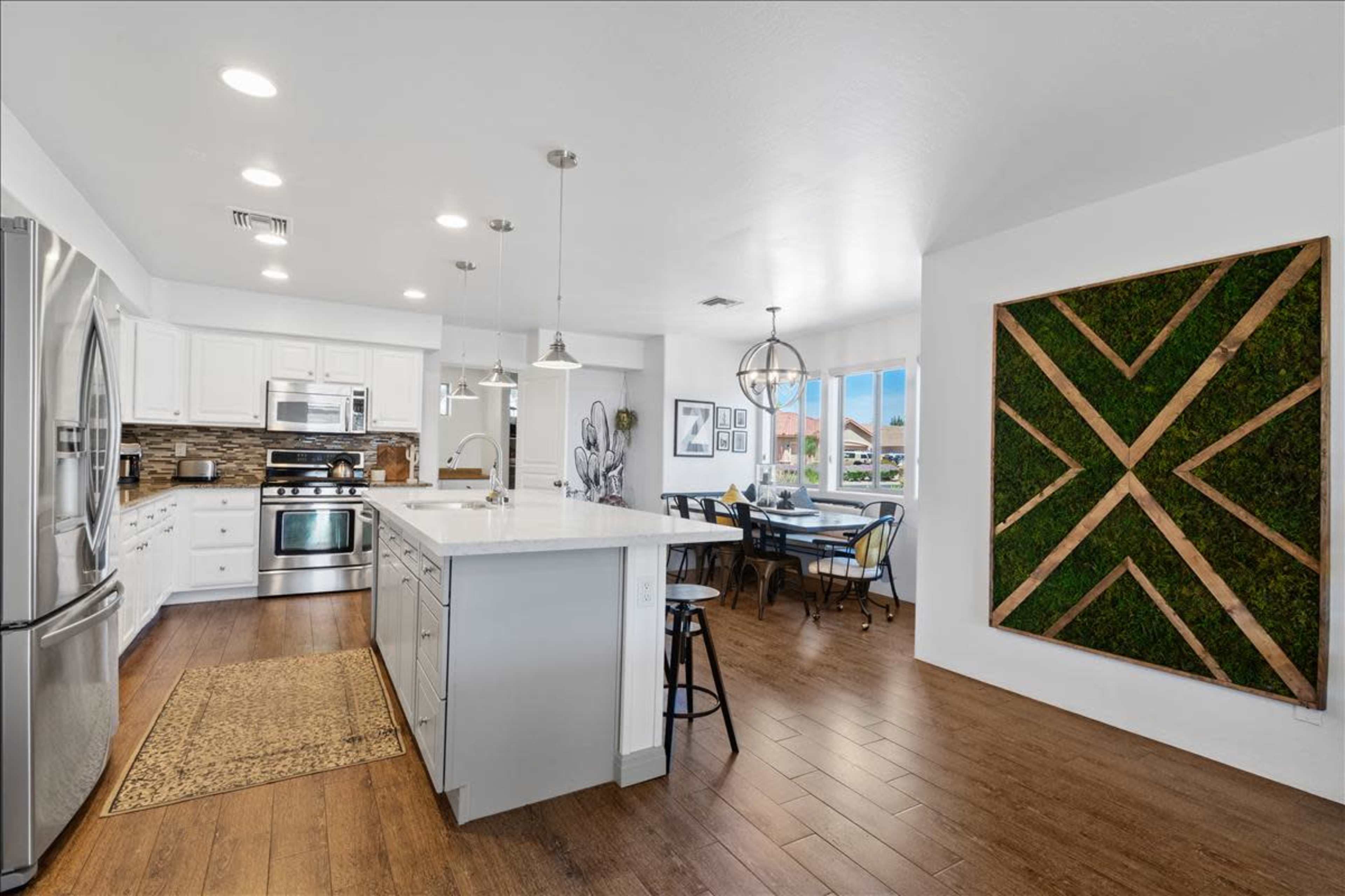 A modern kitchen with white cabinetry, stainless steel appliances, and a dining area featuring a table and chairs near a decorative wall with a green vertical design.