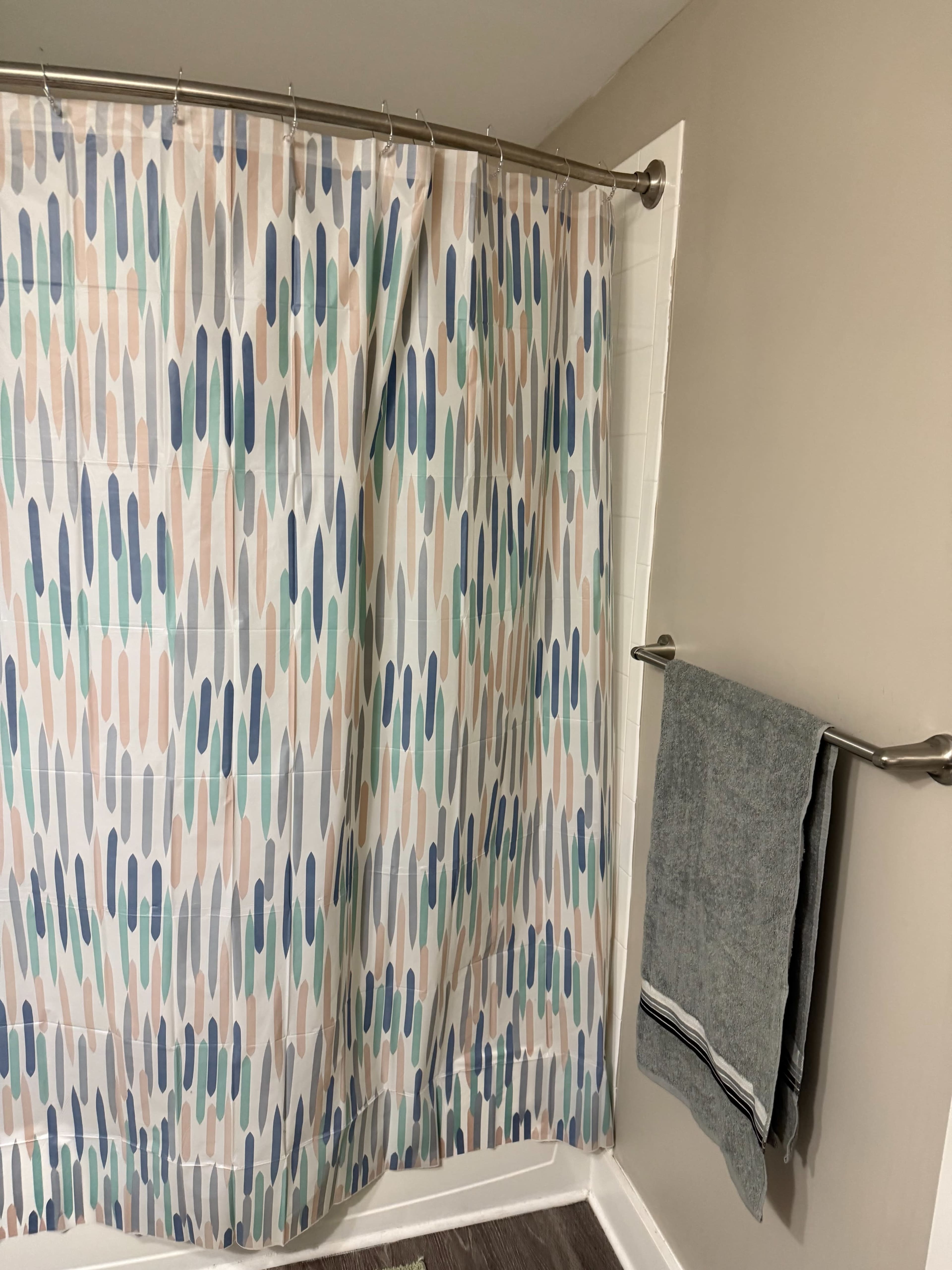 The image shows a bathroom with a patterned shower curtain and a towel hanging on a bar next to the shower.