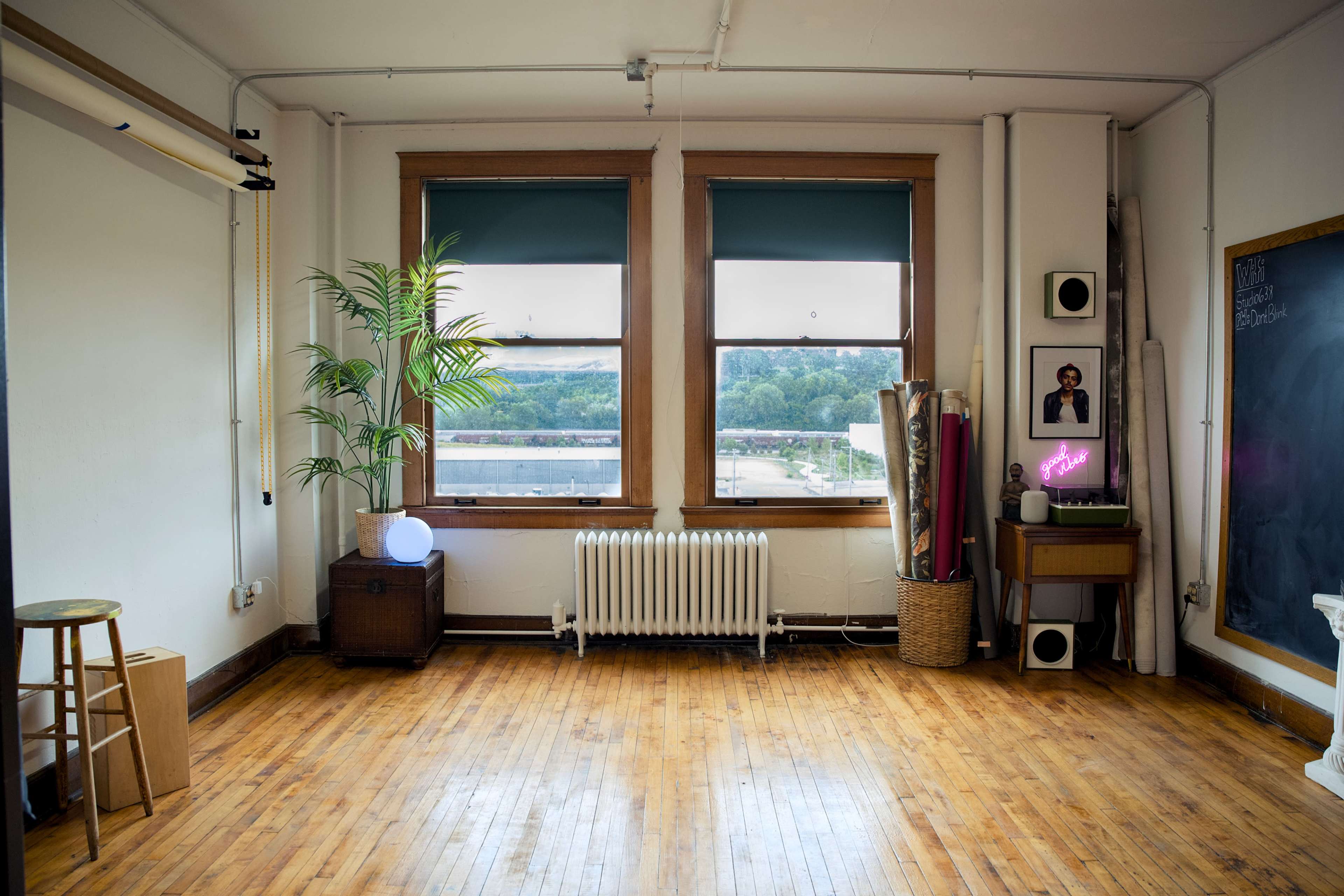 A spacious room with wooden floors, large windows, a potted plant, and various decorative items against the walls.