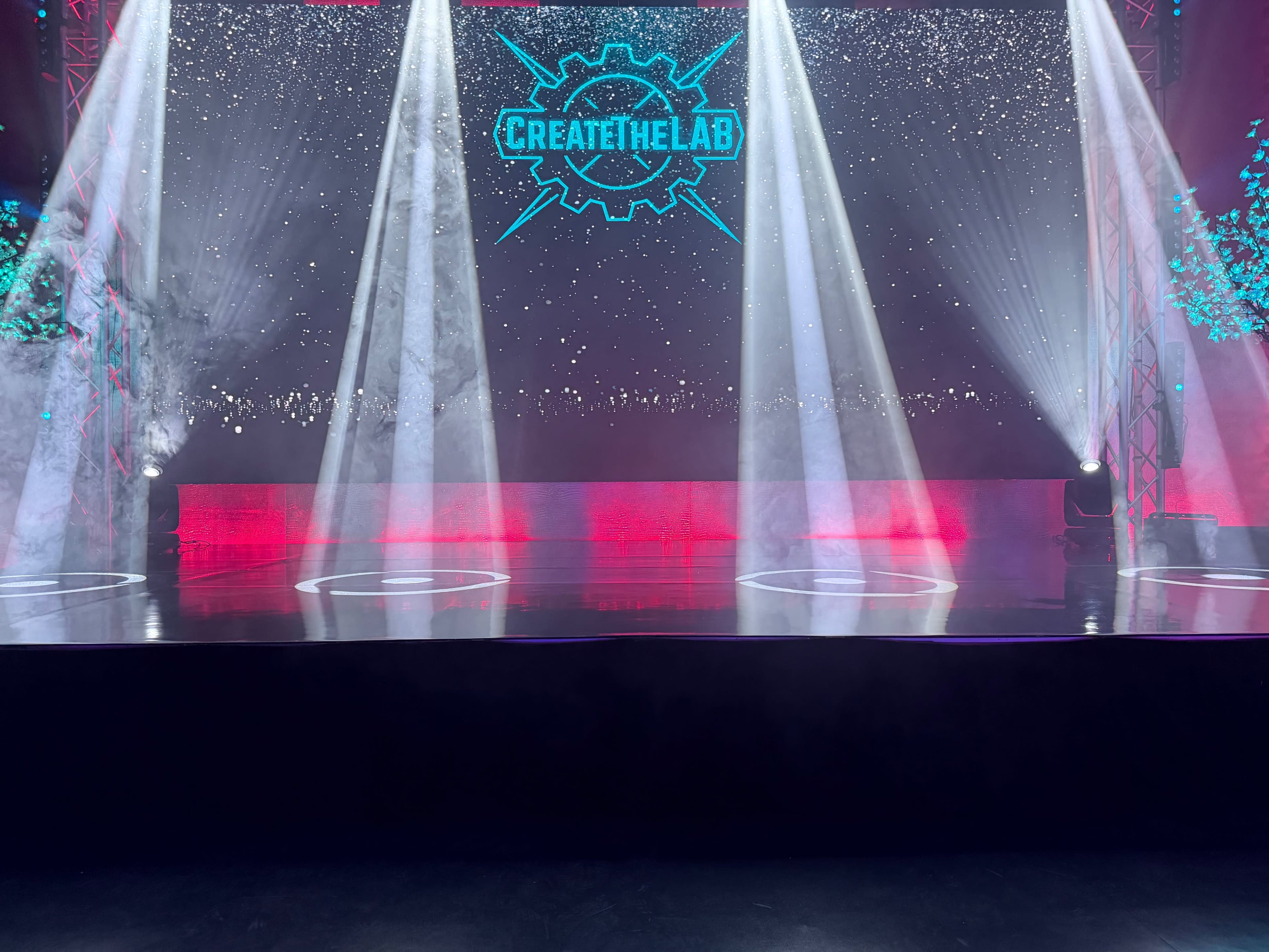 A stage is illuminated with beams of light and a colorful backdrop featuring the words "CREATE THE LAB."
