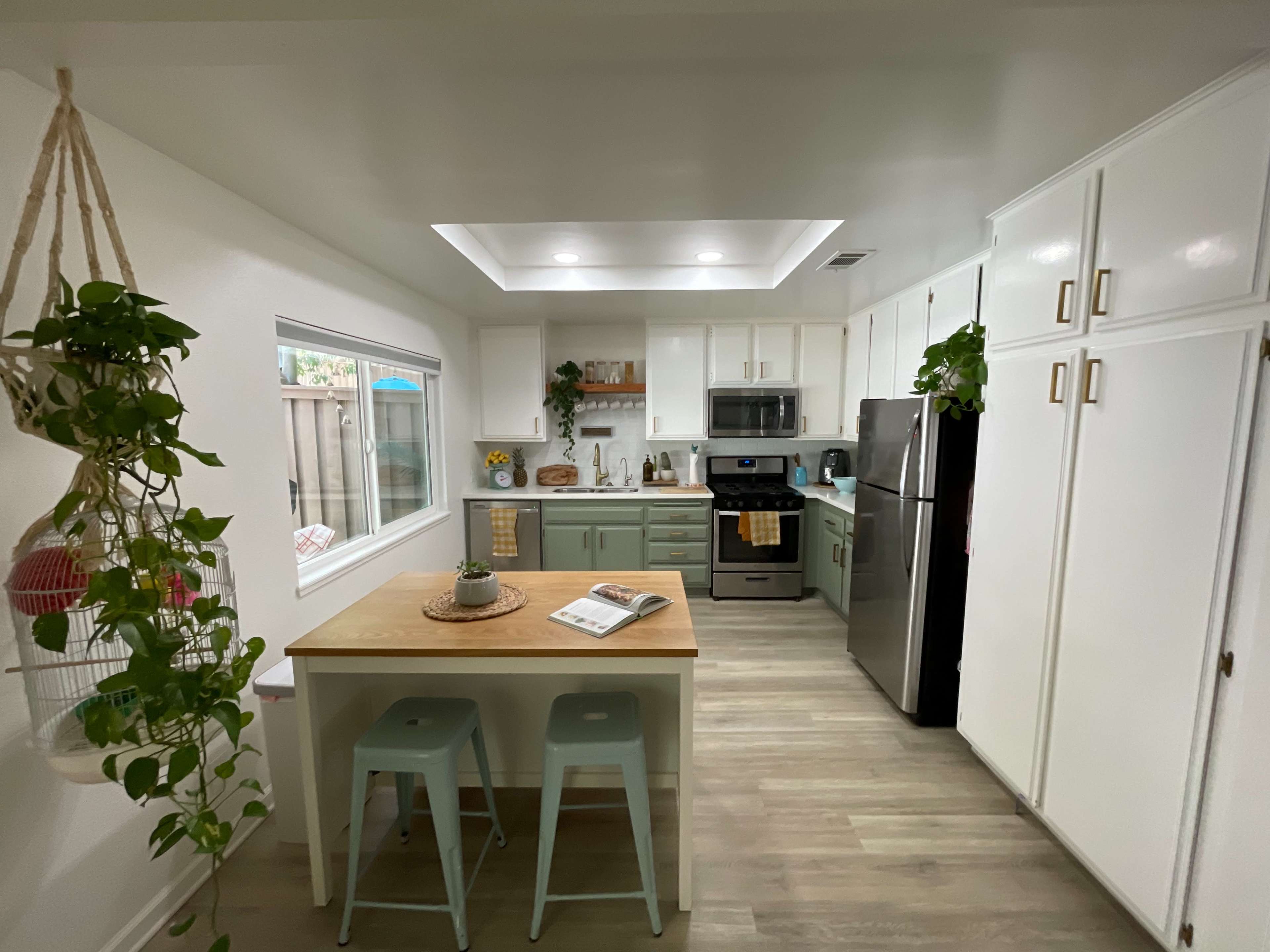 A modern kitchen features light cabinetry, stainless steel appliances, and a small dining area with two stools.