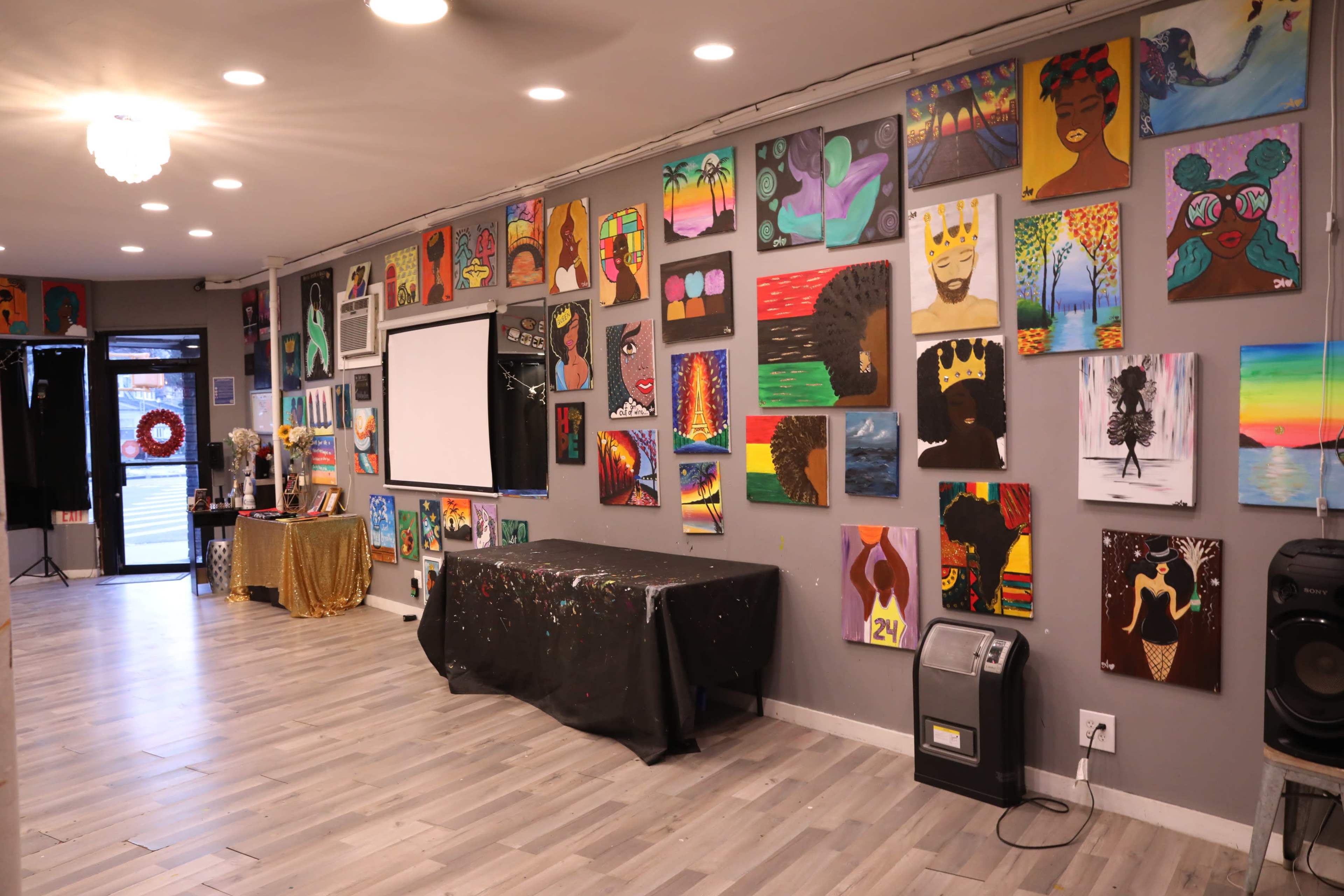 An art gallery interior with a wall adorned with colorful paintings and a projector screen at the front.