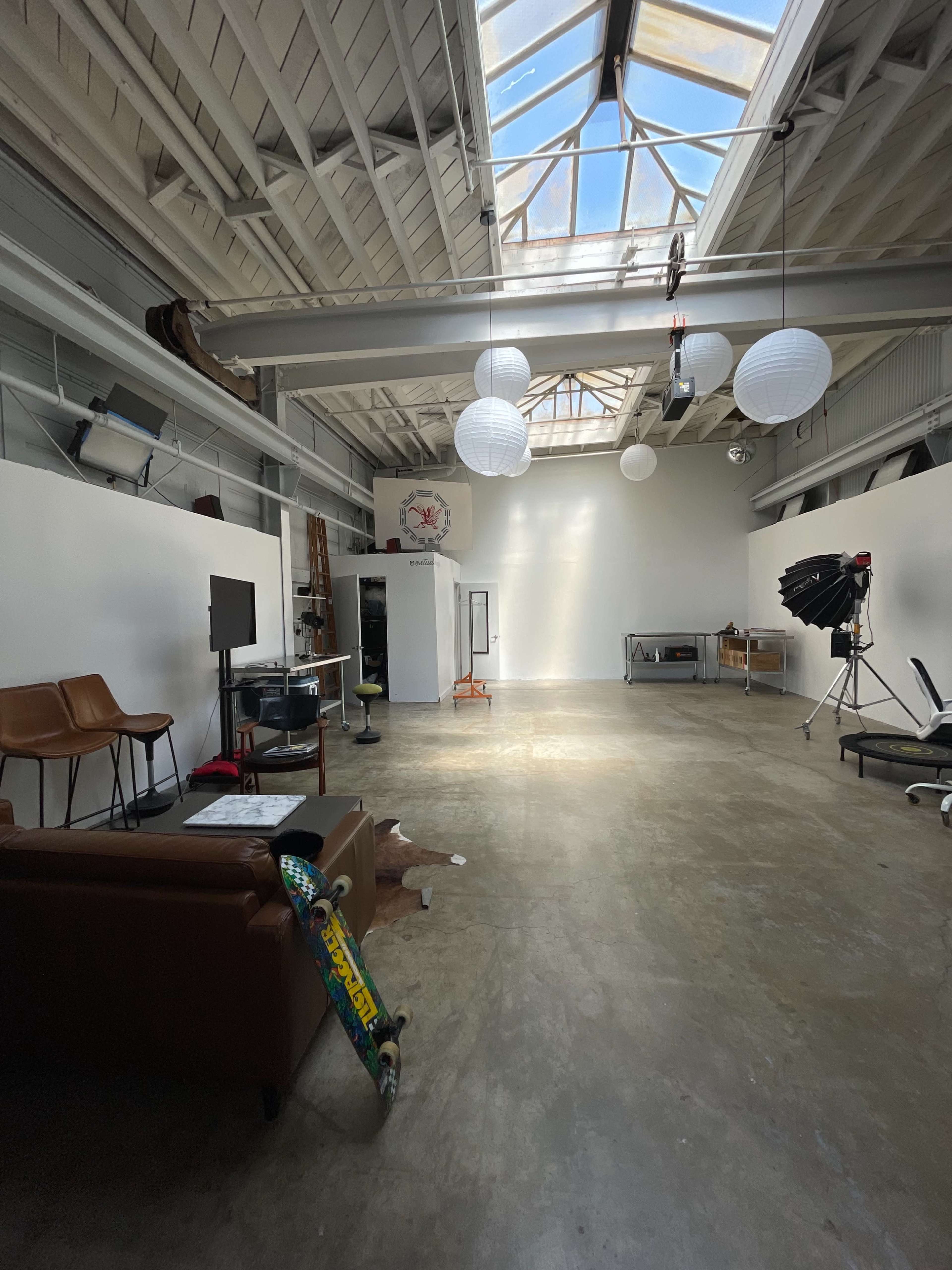 A spacious studio with a high ceiling, large skylights, a seating area, and various equipment scattered throughout.