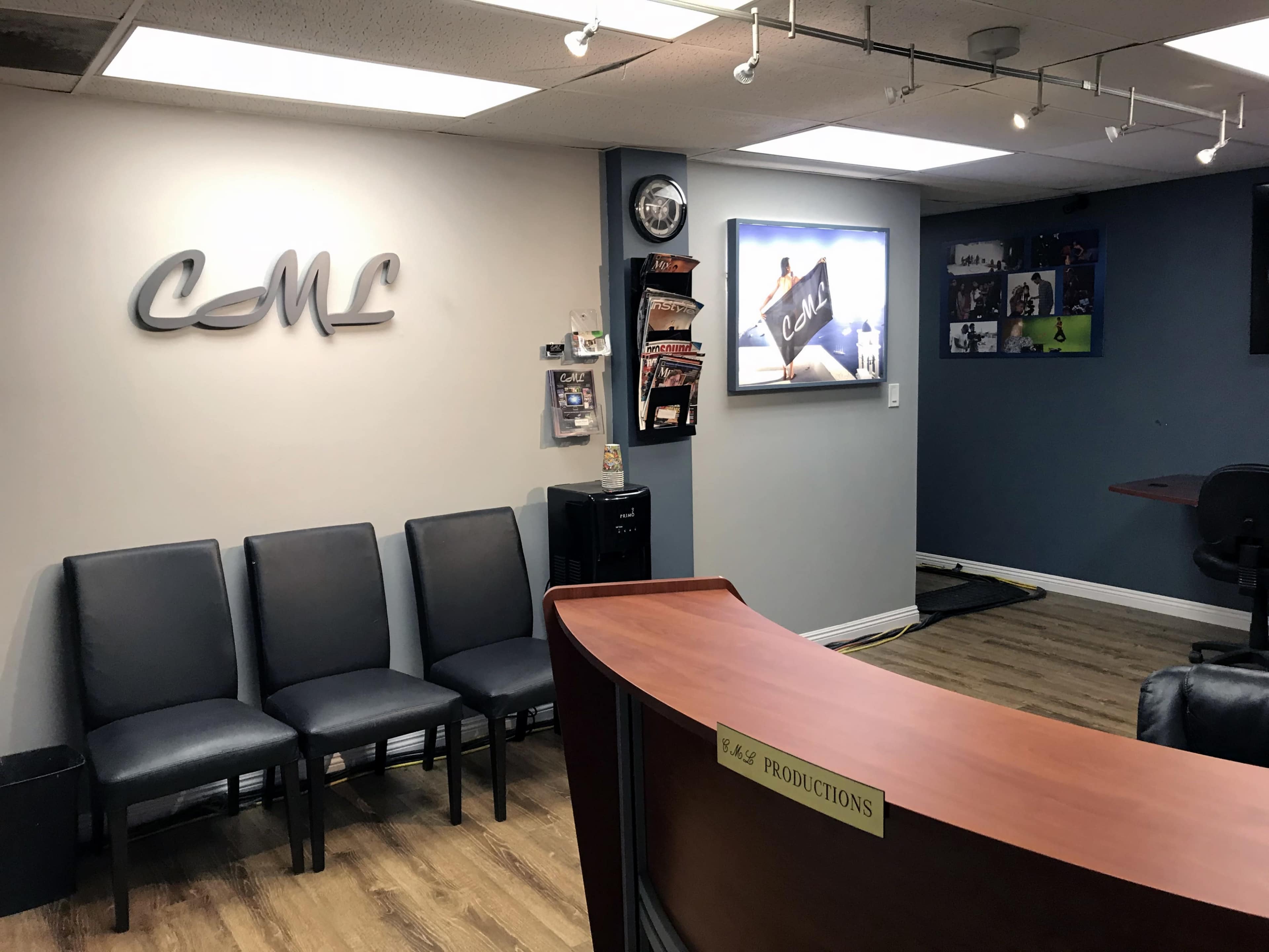 A reception area with a wooden counter, black chairs, and a wall displaying a logo and posters related to a production company.