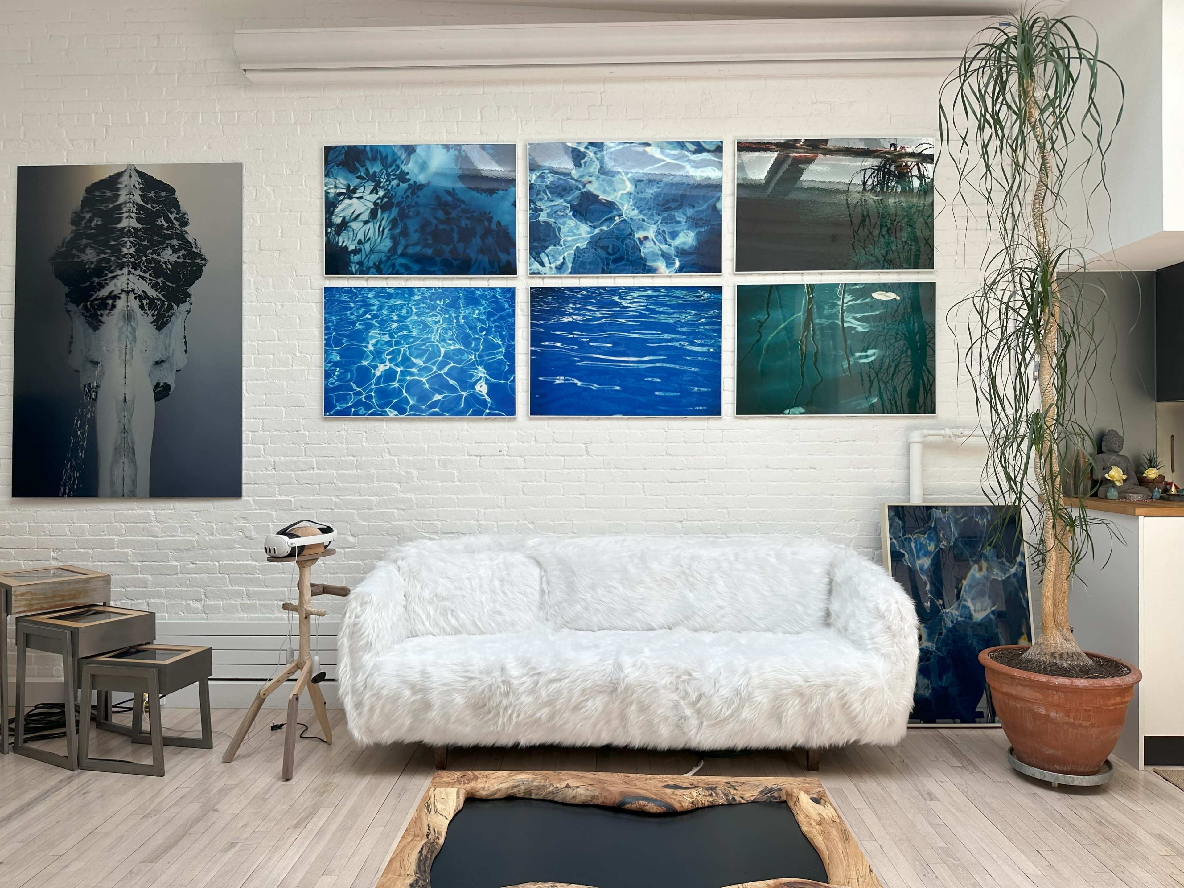 A modern living room with a white fur sofa, a potted plant, and several framed underwater-themed artworks on the brick wall.