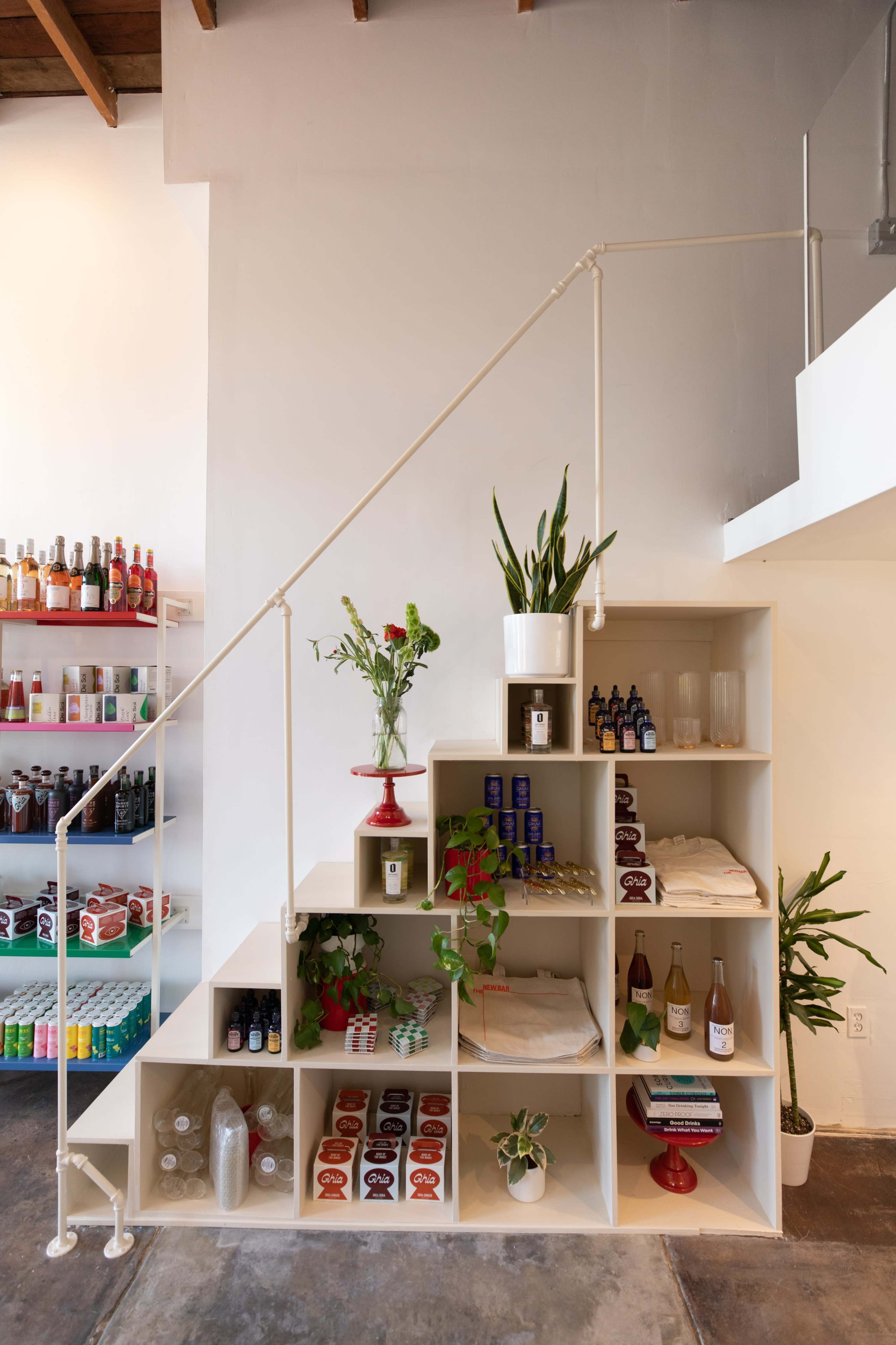A staircase with a white railing leads to an upper level, while the wall beside it features a shelving unit displaying various plants, bottles, and products.