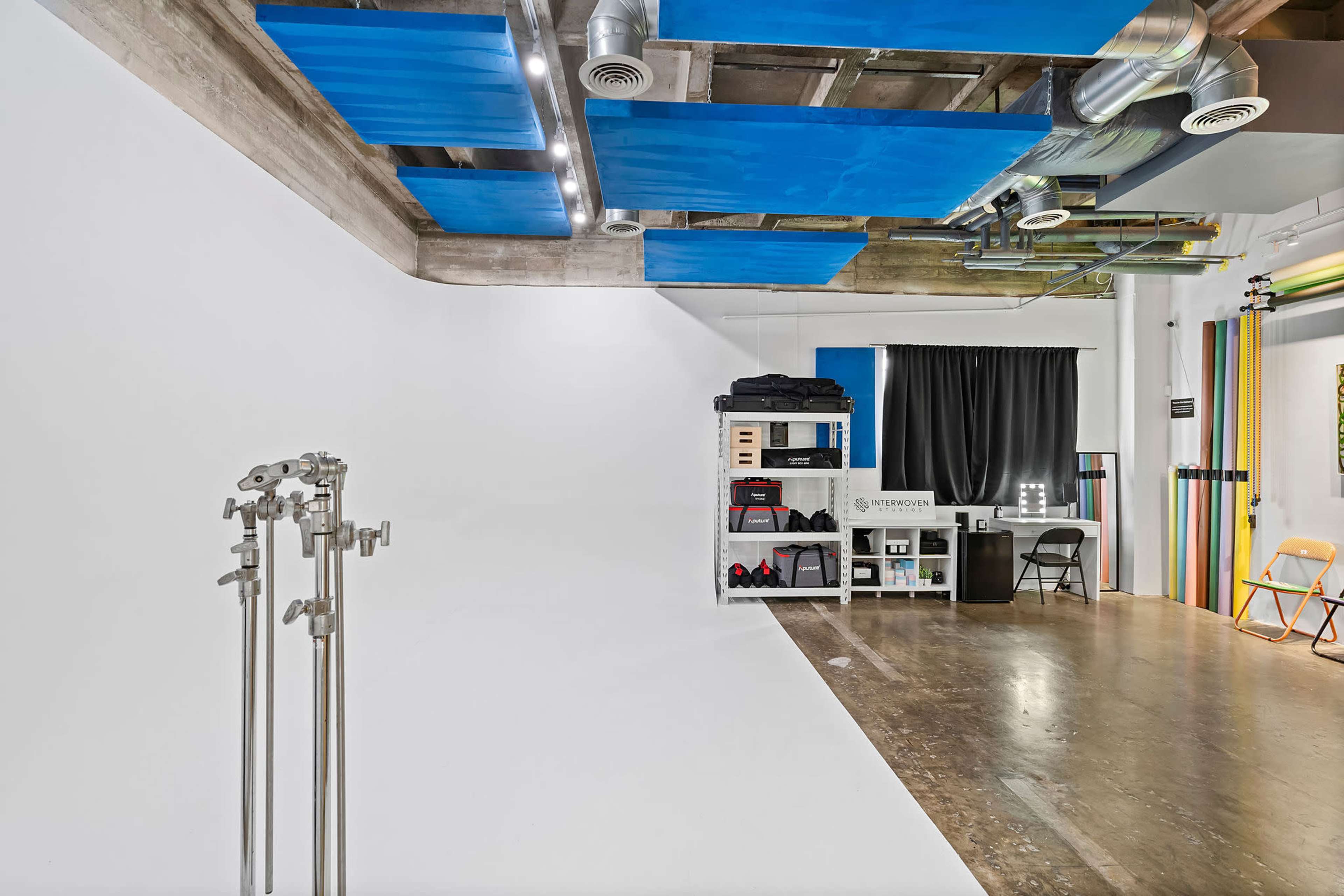 A spacious photography studio with a white backdrop, metal stands, and a shelf displaying various equipment and accessories.