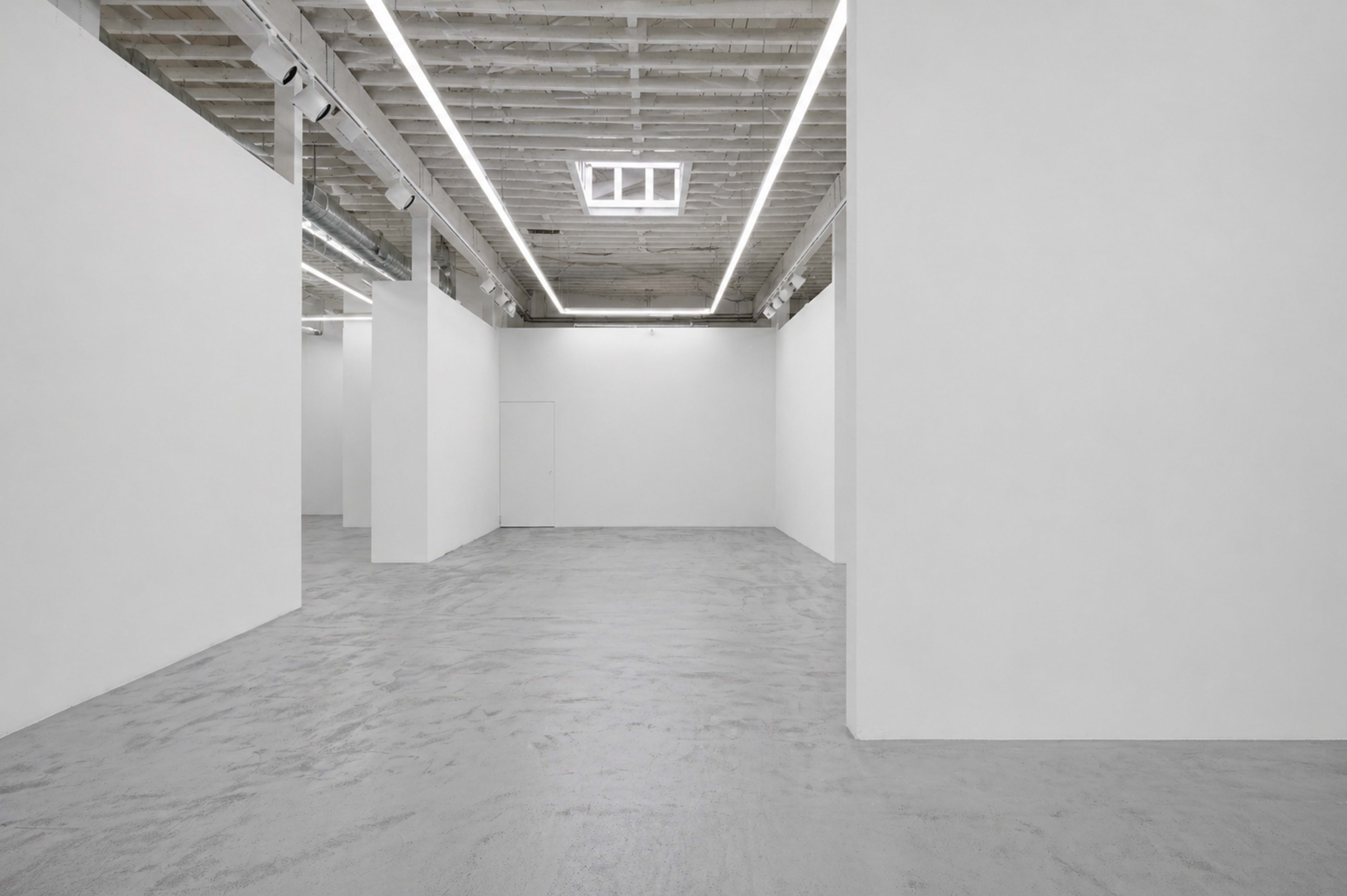 The image shows a spacious art gallery with white walls, a concrete floor, and linear ceiling lighting.