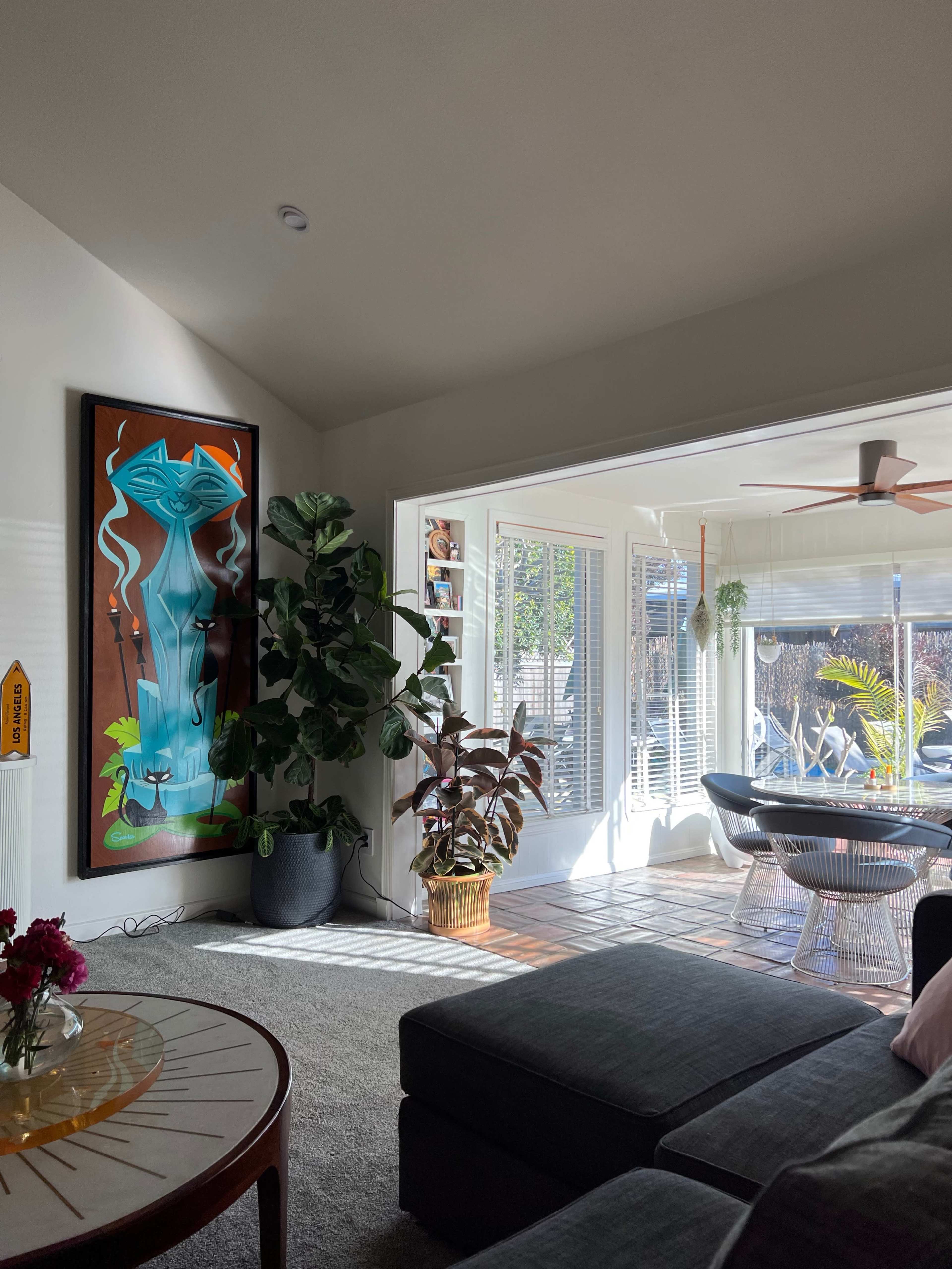 A bright living room featuring a large colorful artwork, a potted plant, and an open area leading to a sunlit patio.