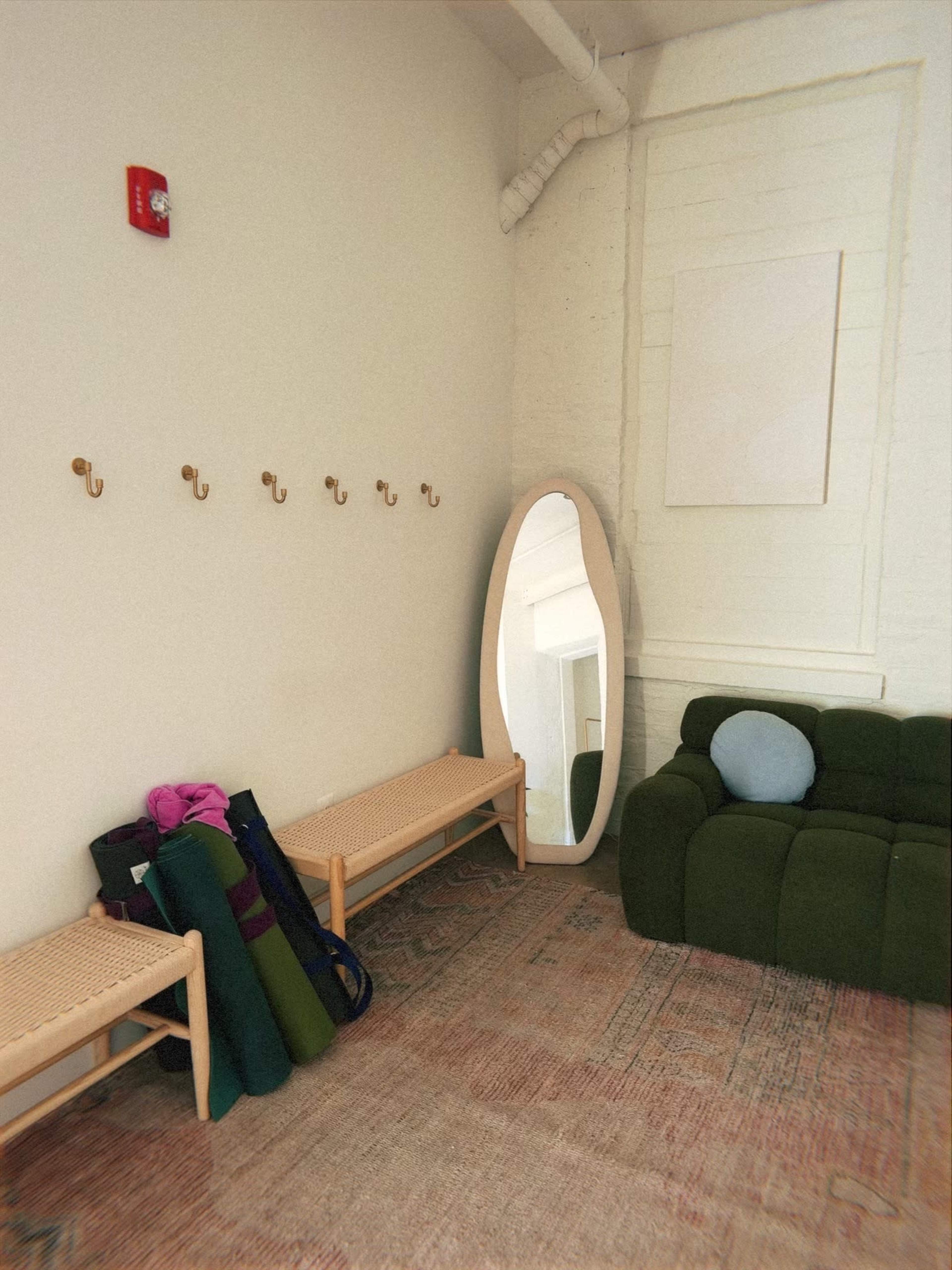 The image shows a minimalist room with two benches, a large oval mirror, yoga mats, and hooks on the wall.