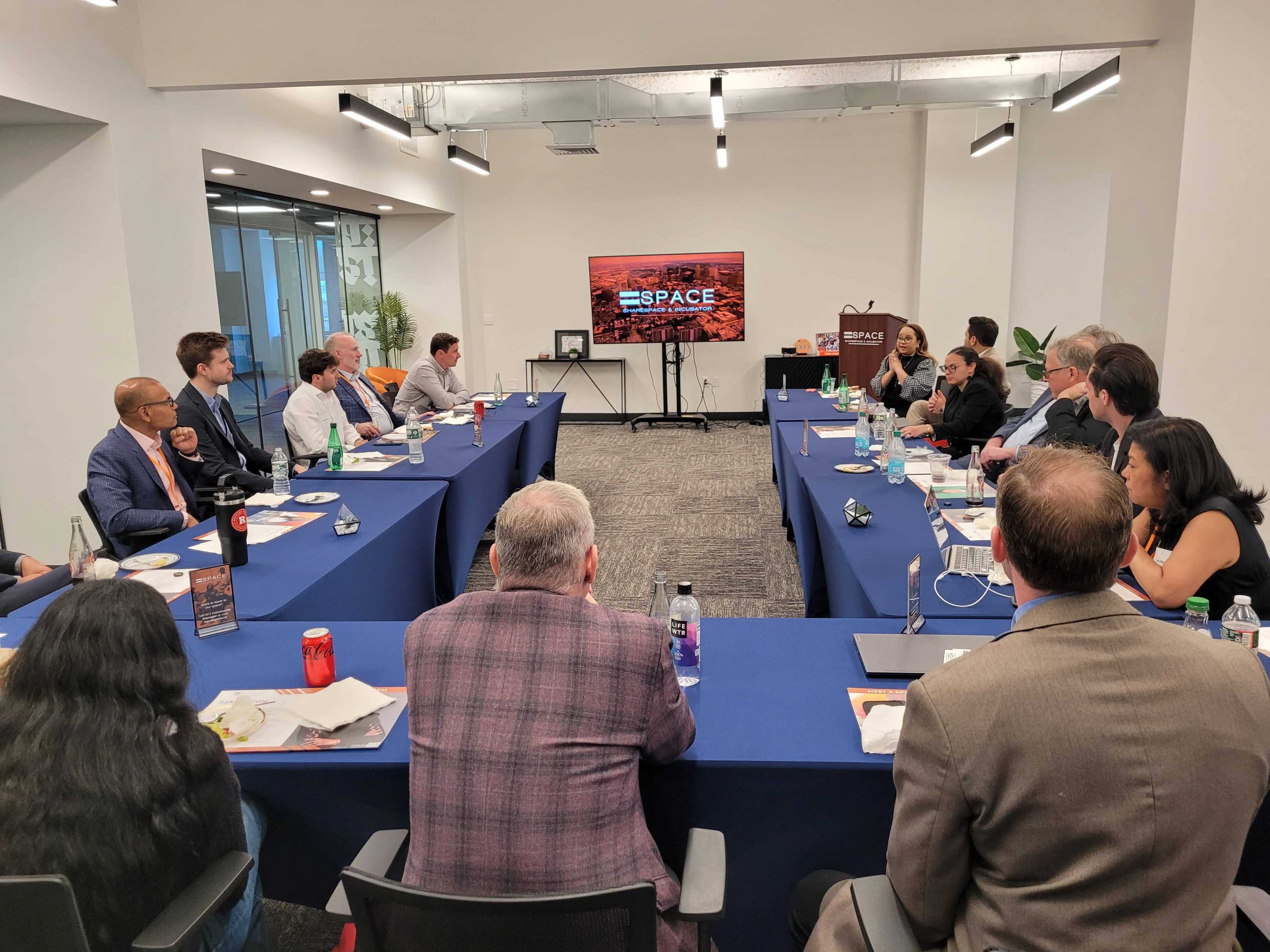 A group of people sits around a long table in a conference room, engaged in a meeting with a large screen displaying the word "SPACE."