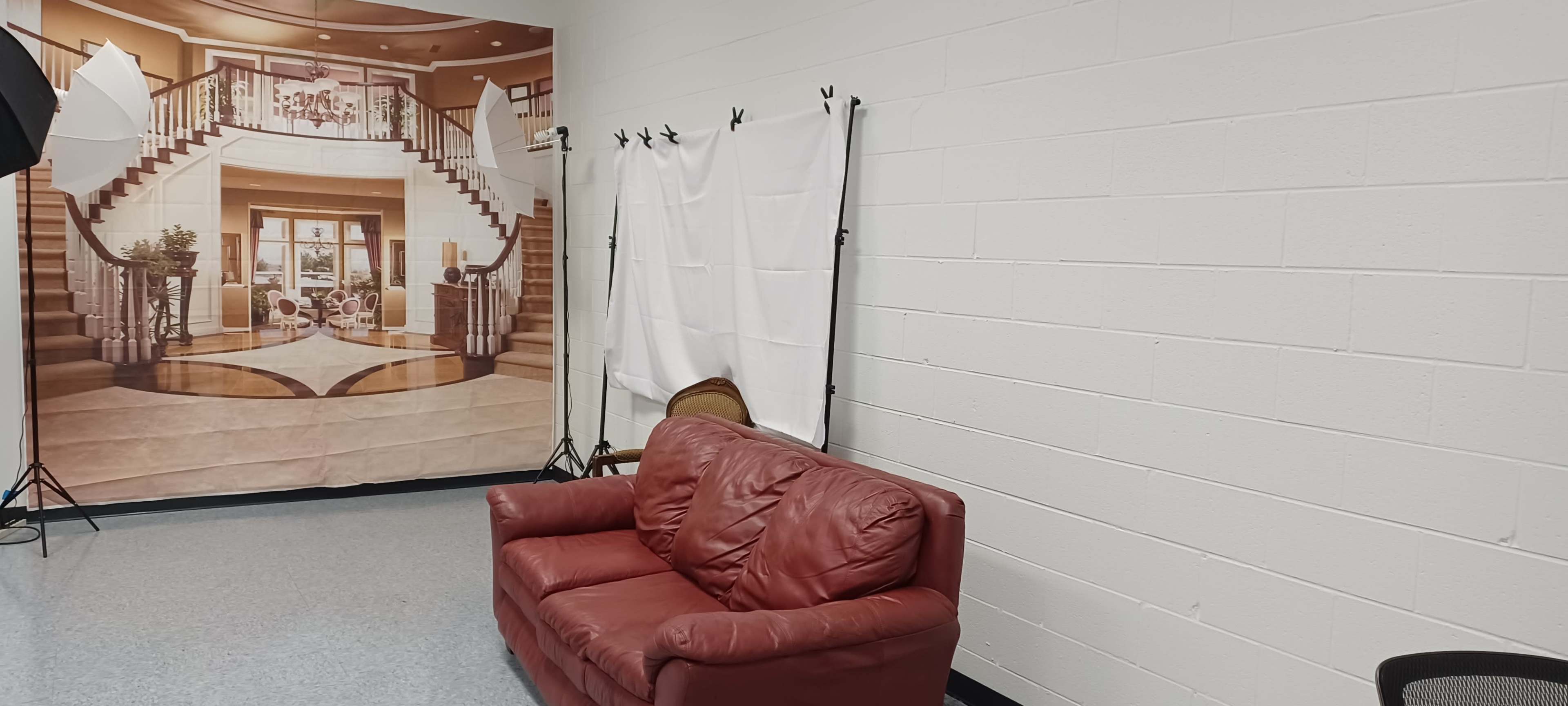 A red leather couch facing a backdrop of a large room with stairs and decor, with white fabric draped on stands nearby.